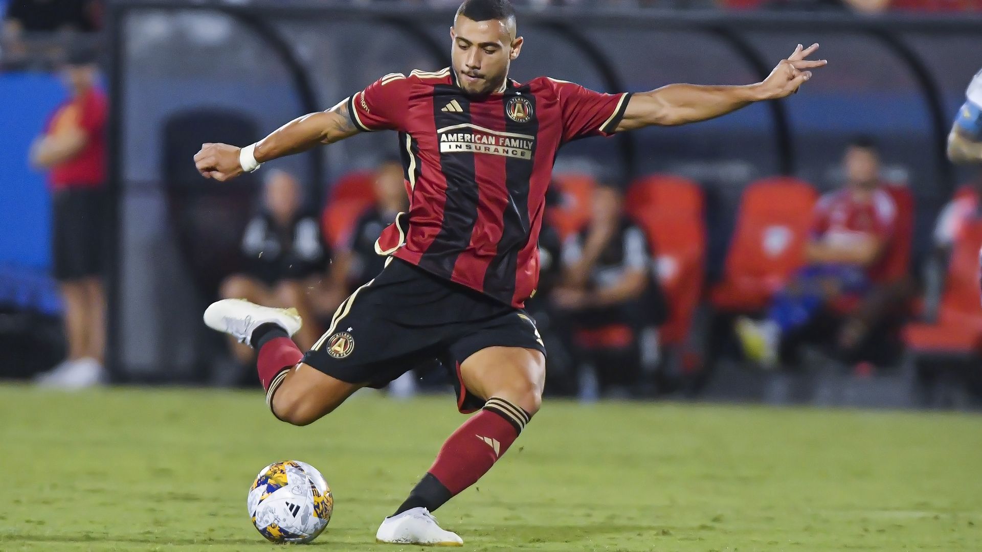 A soccer playing wearing a red-and-black vertical stripe jersey attempts to kick a ball