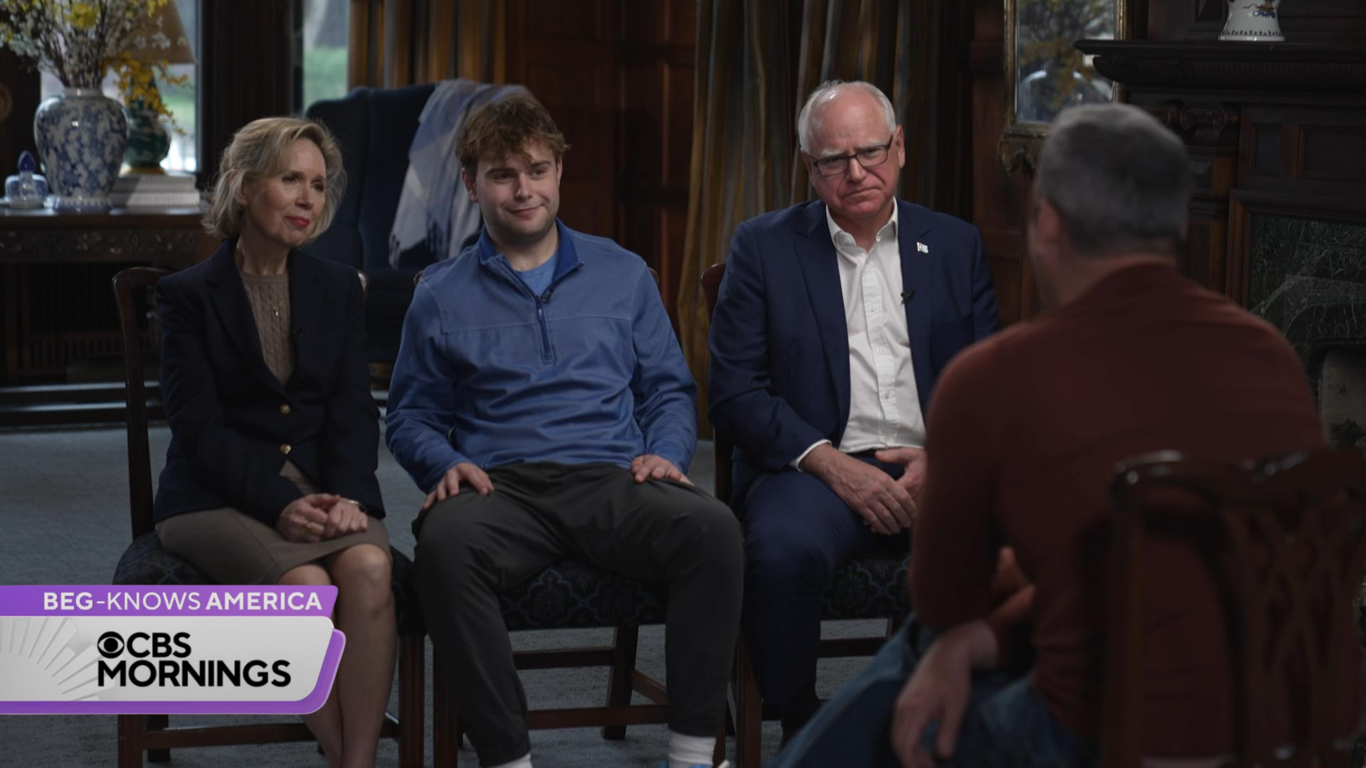 Three people with light skin sit and face an interviewer during a television segment