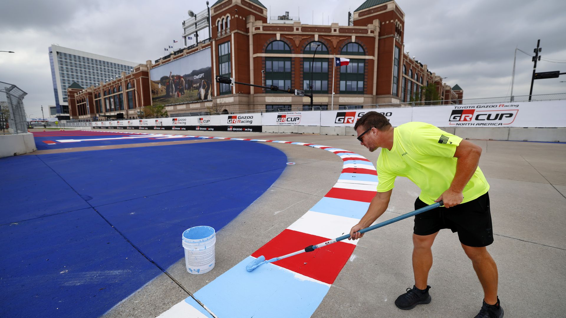 A man paints a rumble strip on a race track in front of Choctaw Stadium