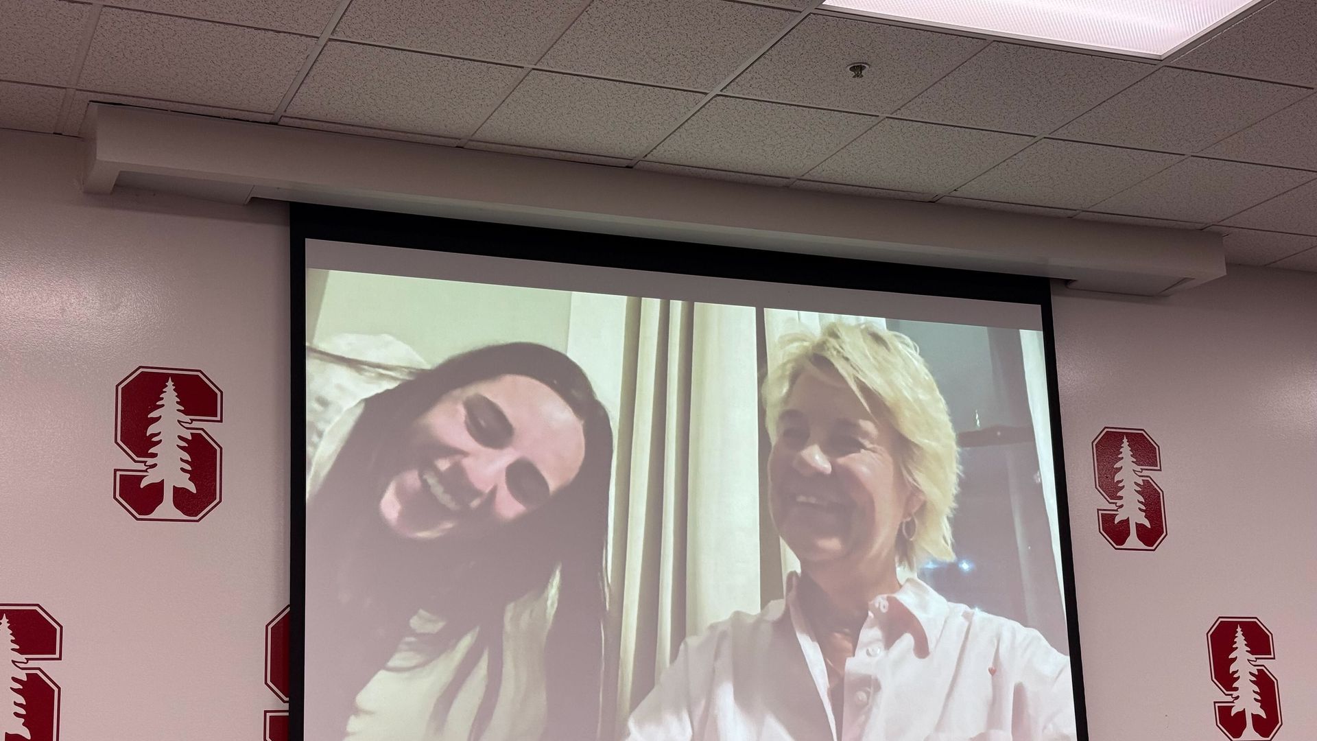 A large screen in a Stanford extension classroom showing Caitlin Clark and her college coach Lisa Bluder (via Zoom).