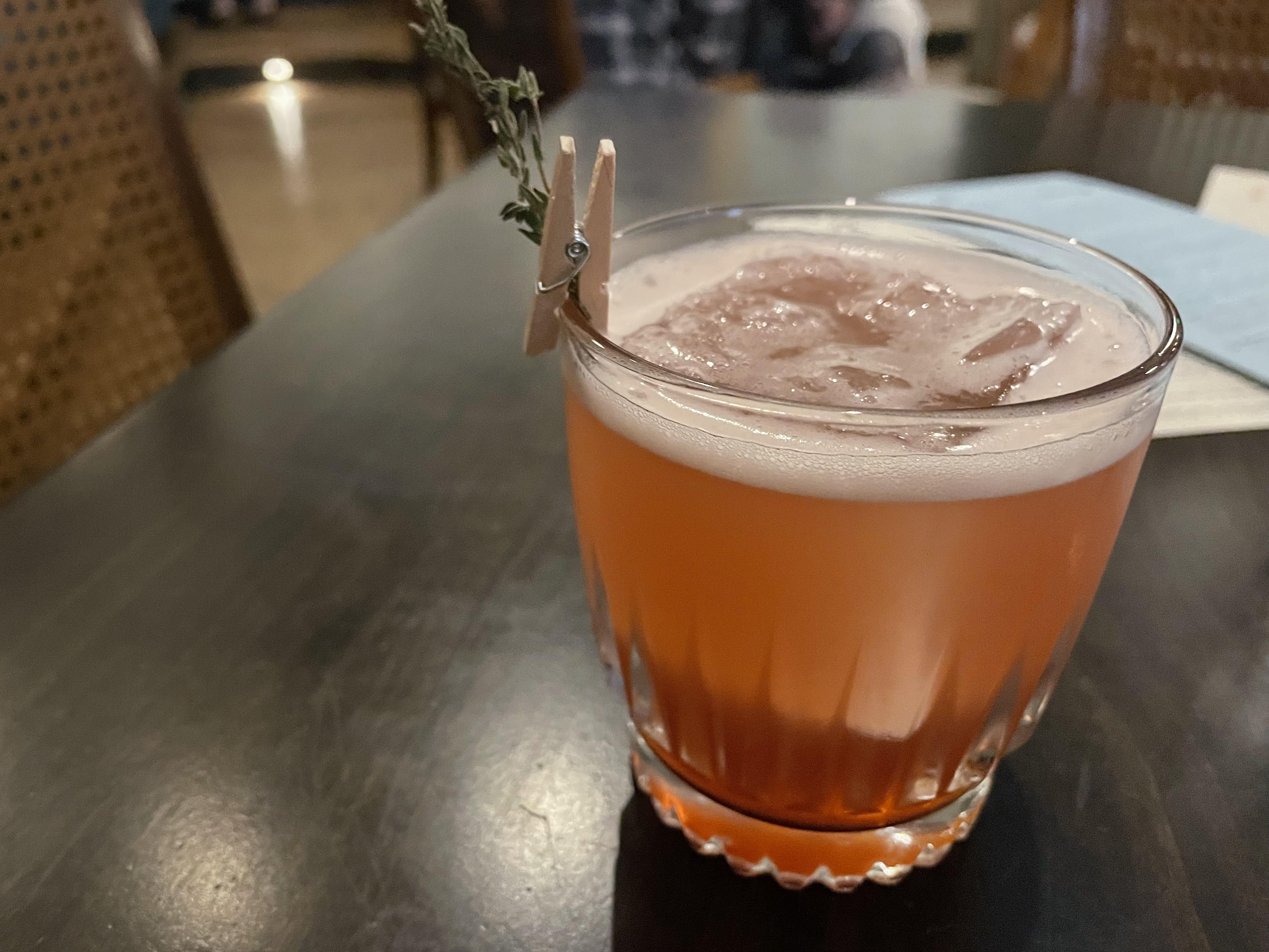 glass filled with orange-pink colored liquid and large ice cube floating at the top.