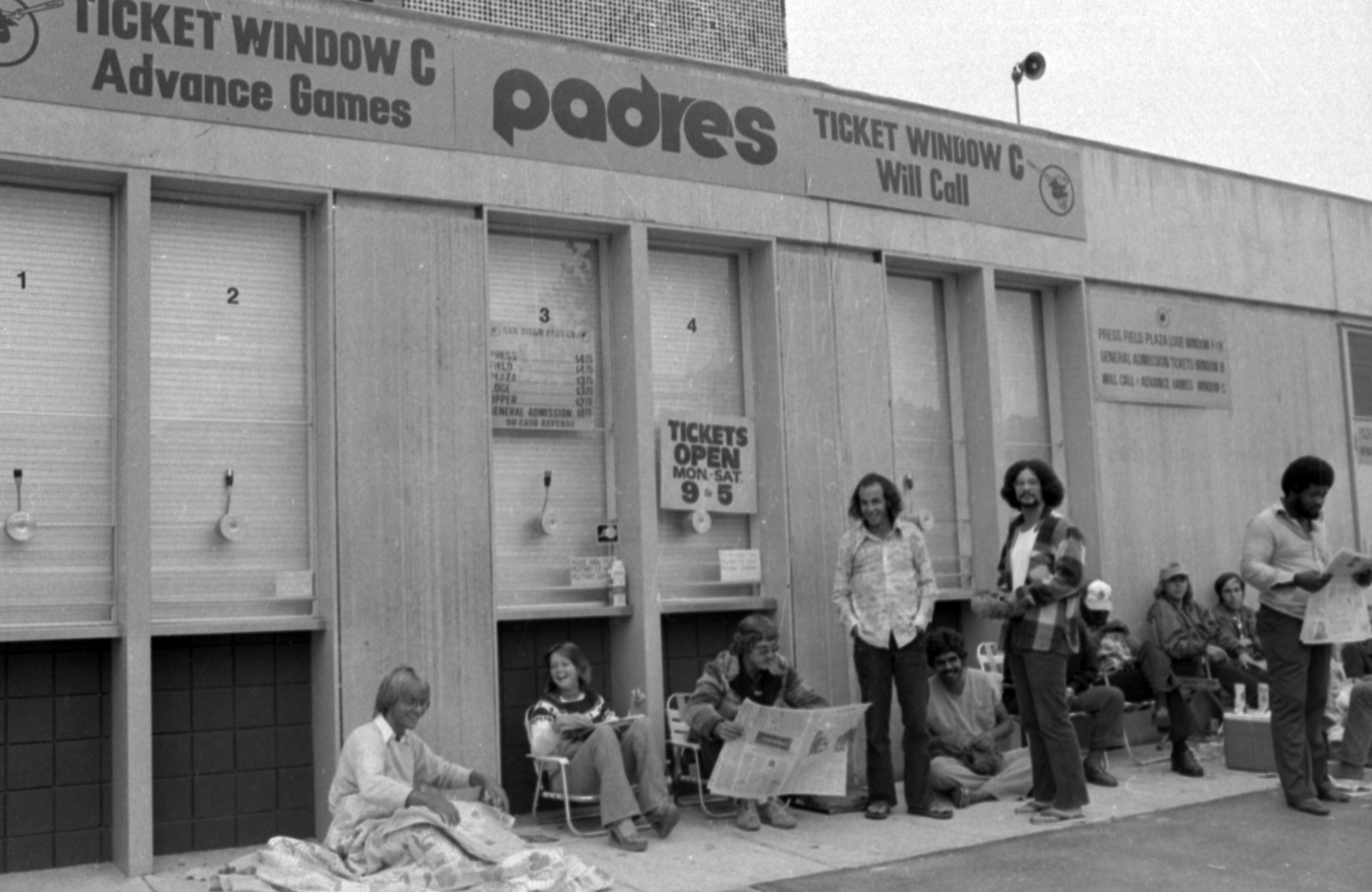 Black-and-white photo of a row of Padres ticket windows with a large 'Padres' sign; signs read 'Ticket Window C' and 'Will Call'. People stand and sit outside, some holding newspapers.
