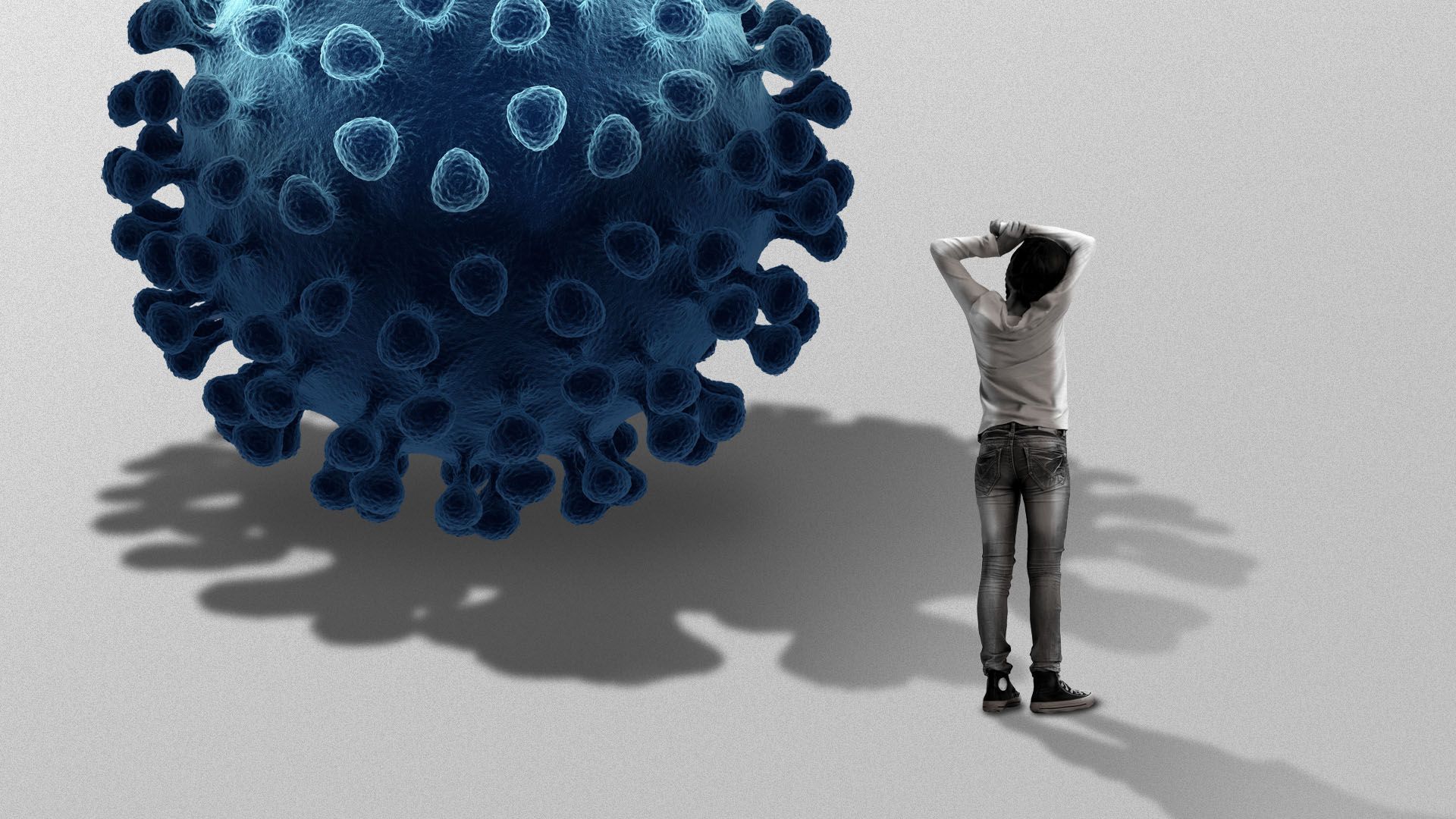 A person with their arms rested on their head stands beside a giant virus particle.