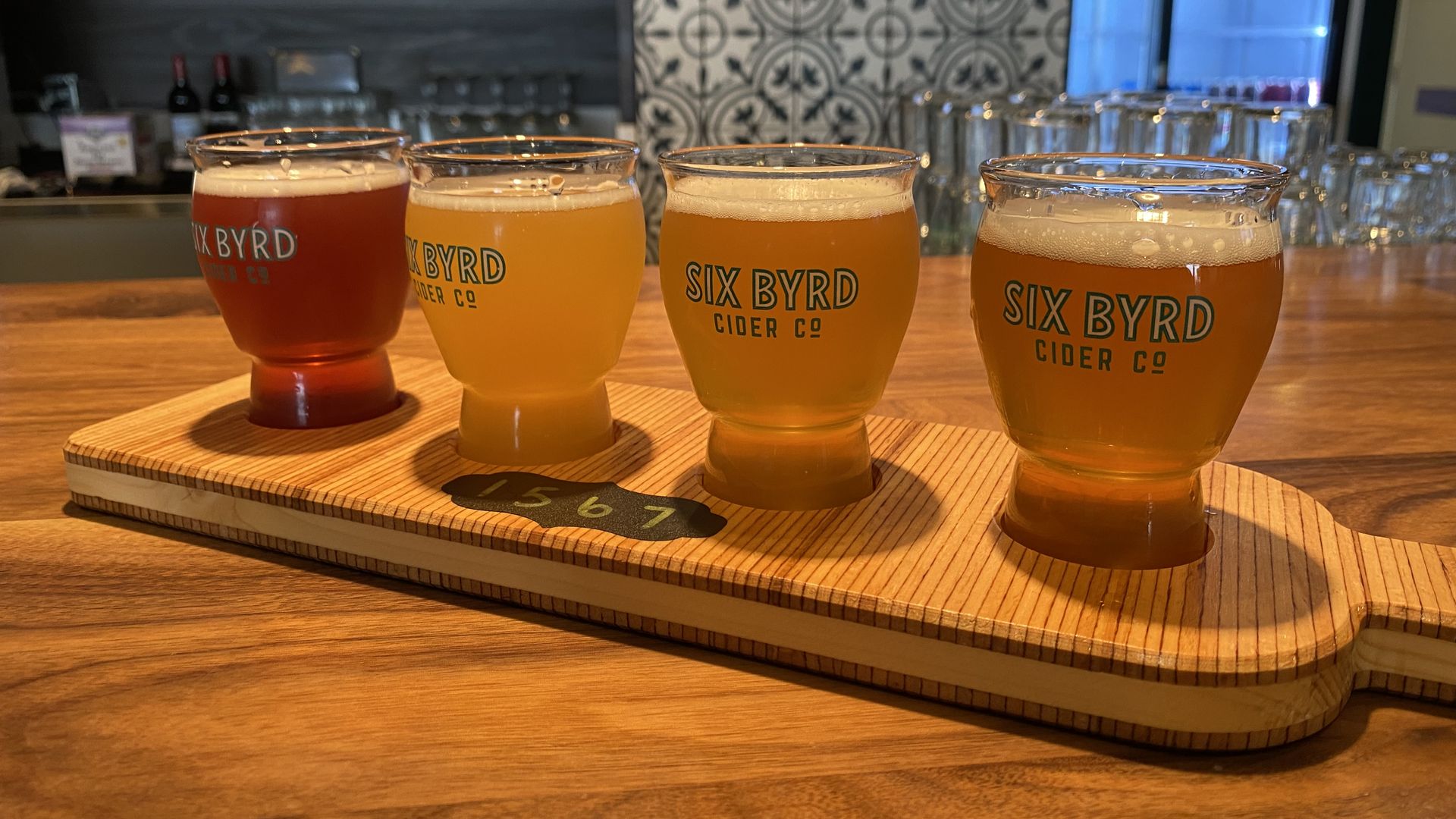 Four small glasses of hard cider arranged on a wooden board
