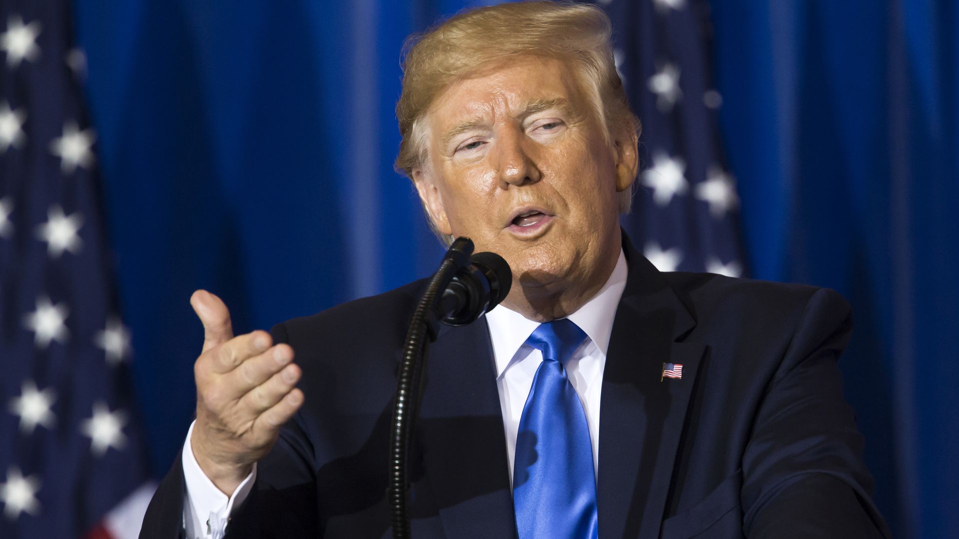 Trump standing at a podium and gesturing forward.
