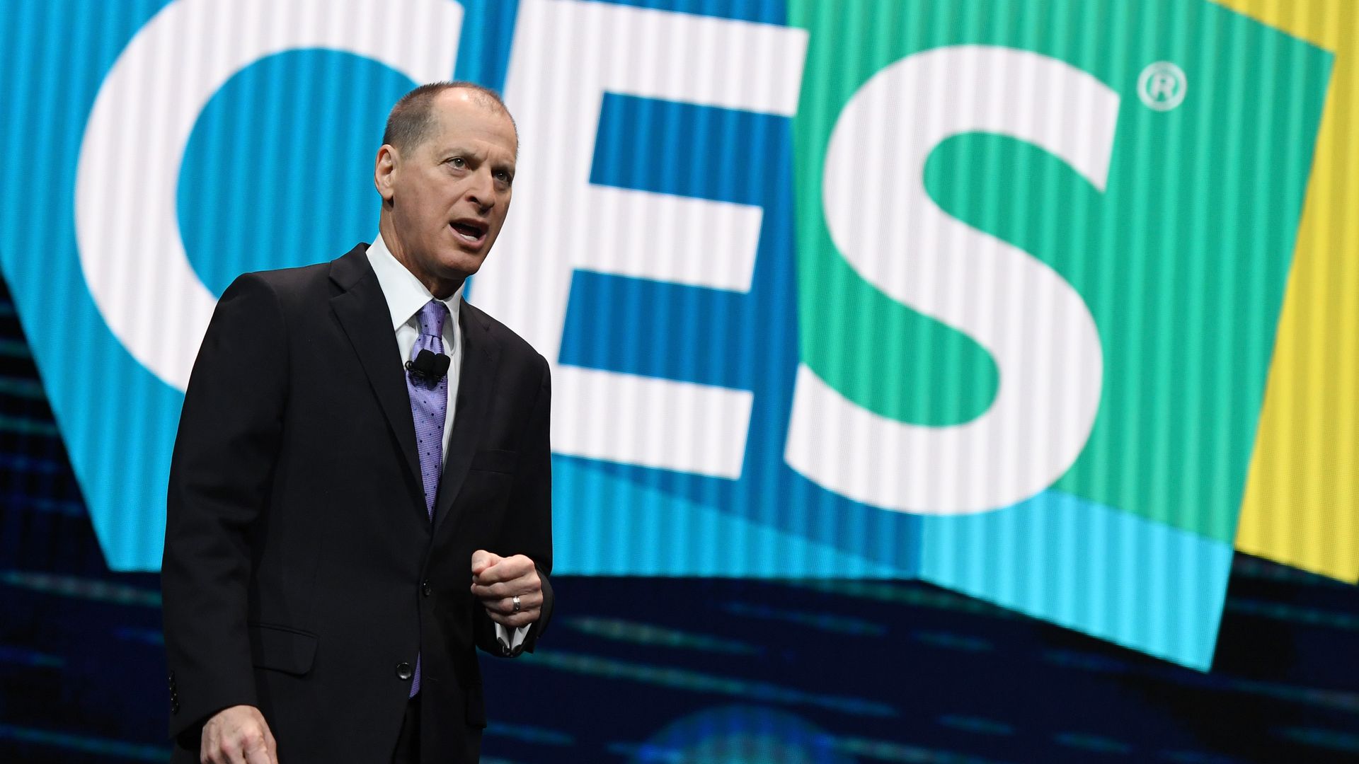 Gary Shapiro wears a suit on stage, in front of a CES logo