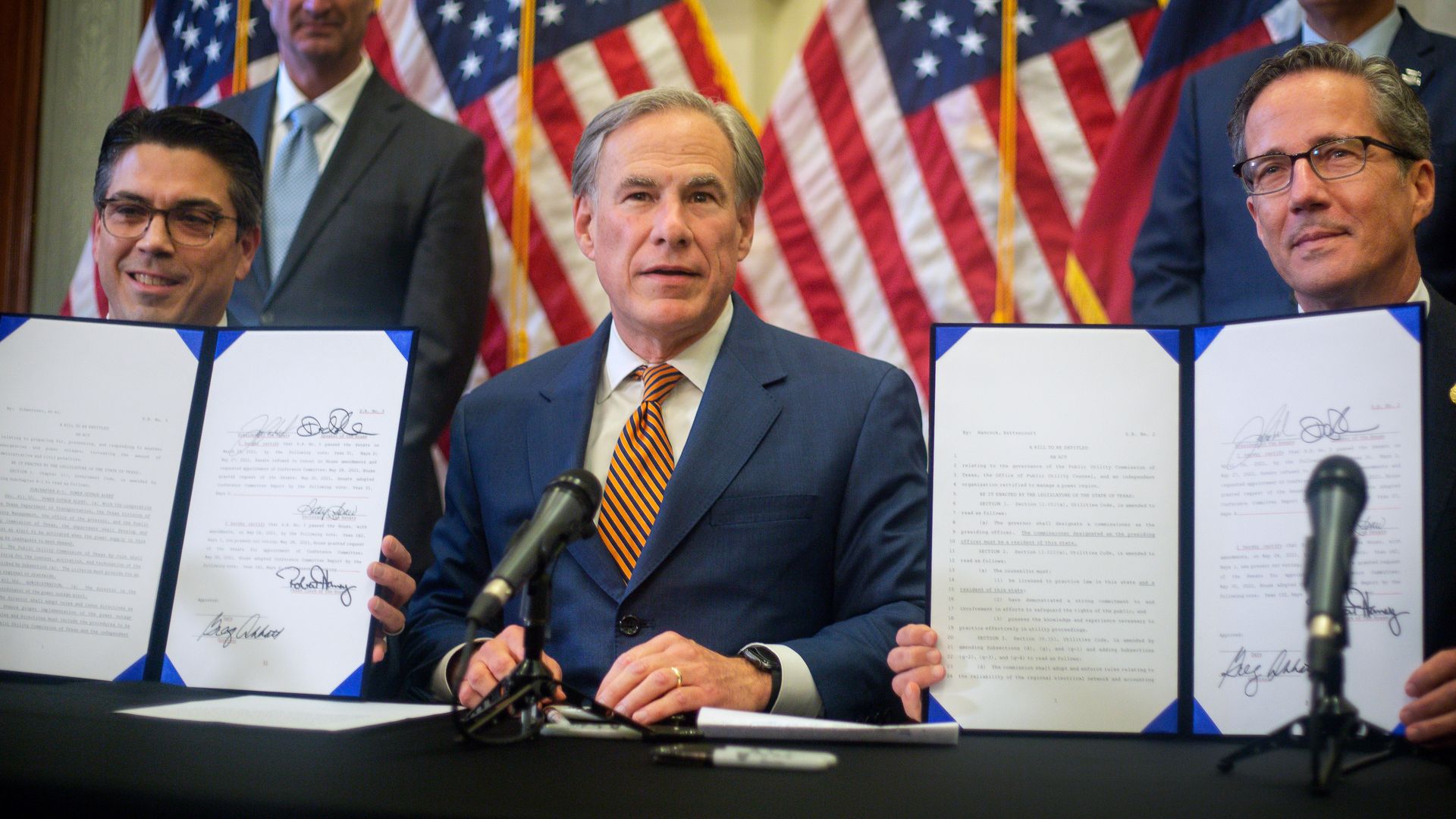 Photo of Greg Abbott sitting between two people holding up bills he just signed