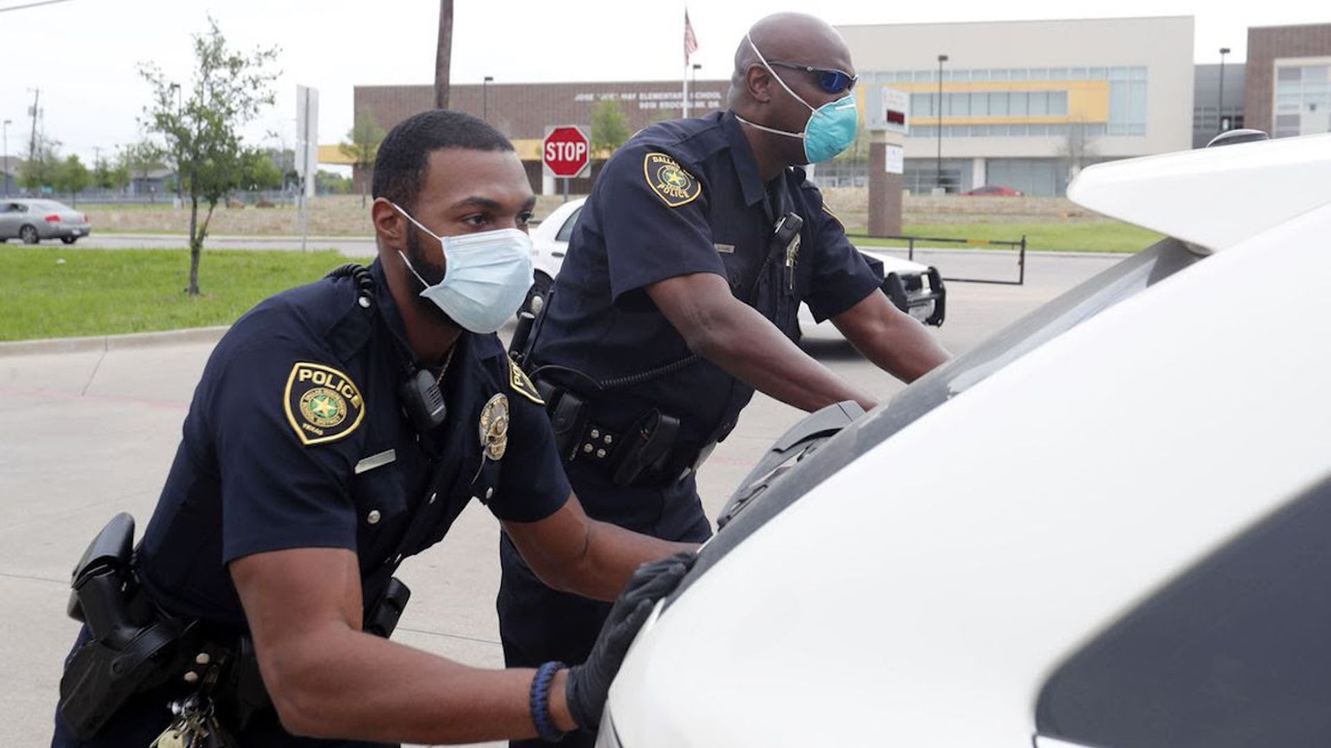 Dallas school district officers Mylon Taylor and Gary Pierre push a car that ran out of gas while waiting in line for a weekly school meal pick-up.