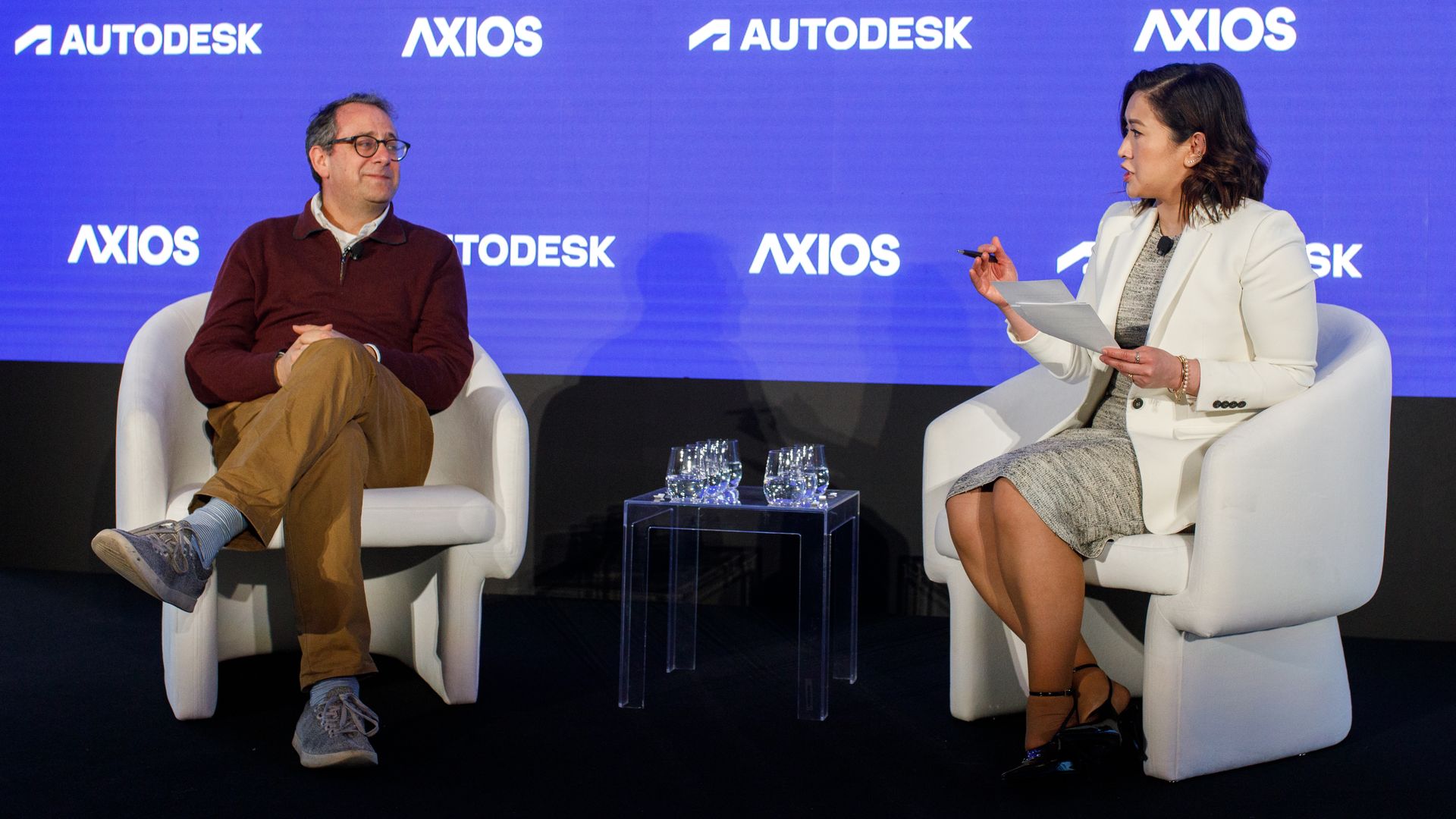 man sitting on chair on a stage next to a woman who is interviewing him