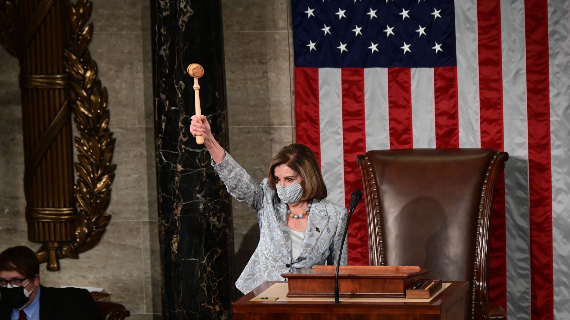Nancy Pelosi holds up a gavel while standing in front of an American flag