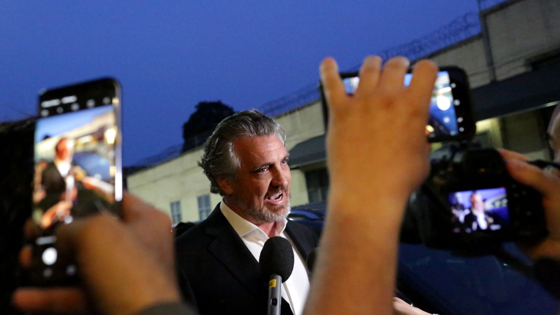 In this image, Del Bigtree speaks to a crowd of reporters who hold up camera phones. 