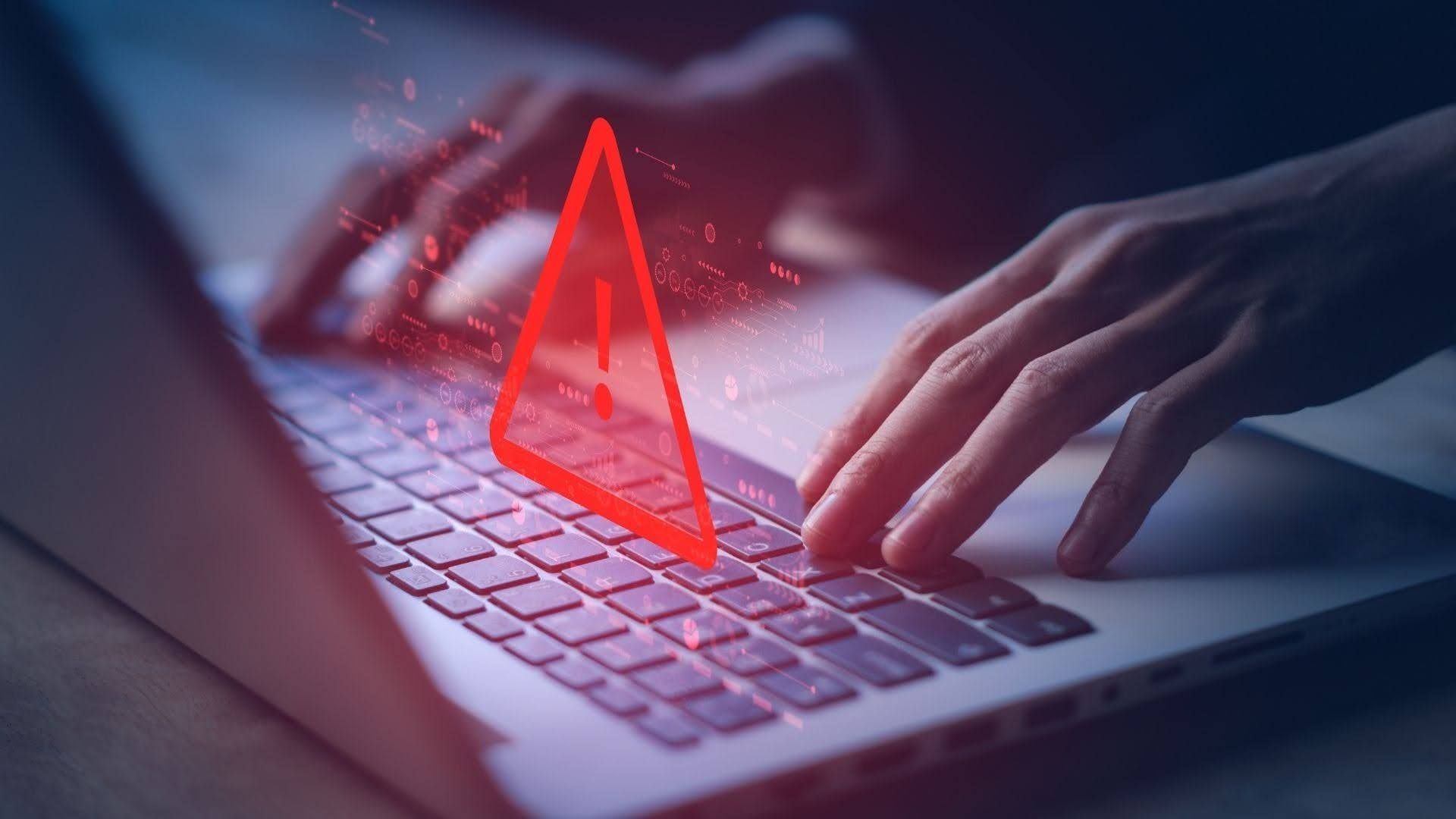A person typing on a laptop keyboard with a bold red warning triangle overlaid, and red glowing data graphics in the background, suggesting a cybersecurity alert.