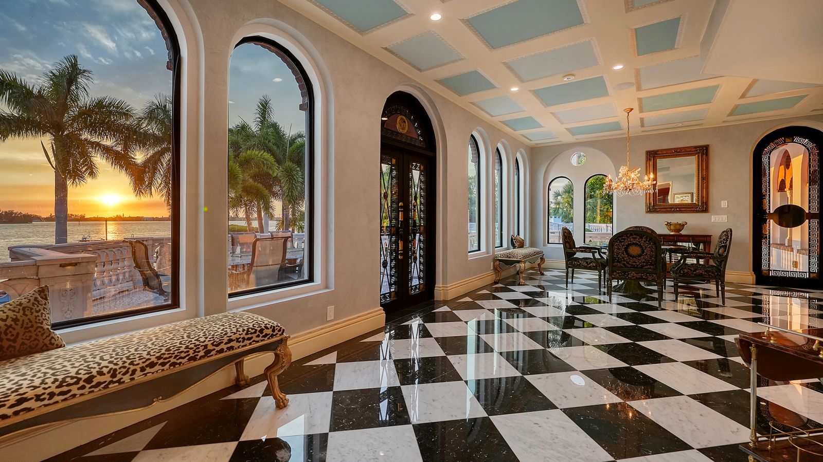 A room with black-and-white marble floors and an arched window overlooking a sunset over the water.