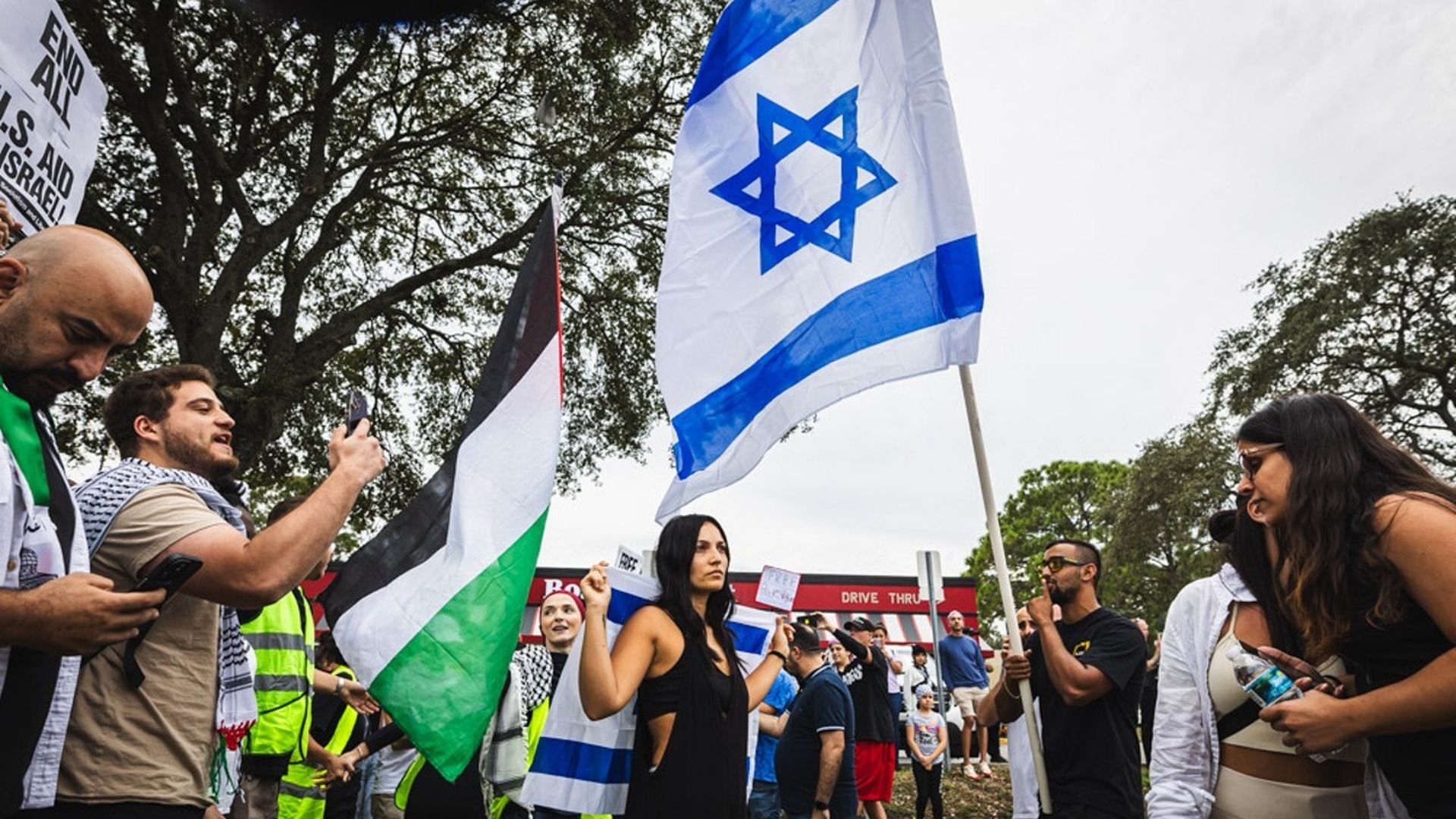 People holding Palestine flags and Israli flags argue outside a boston market