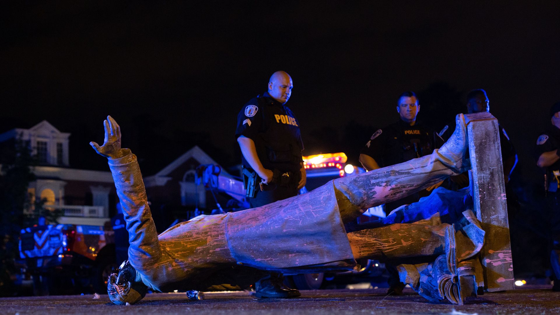 Two police officers stand over a fallen Jeff Davis statue. 