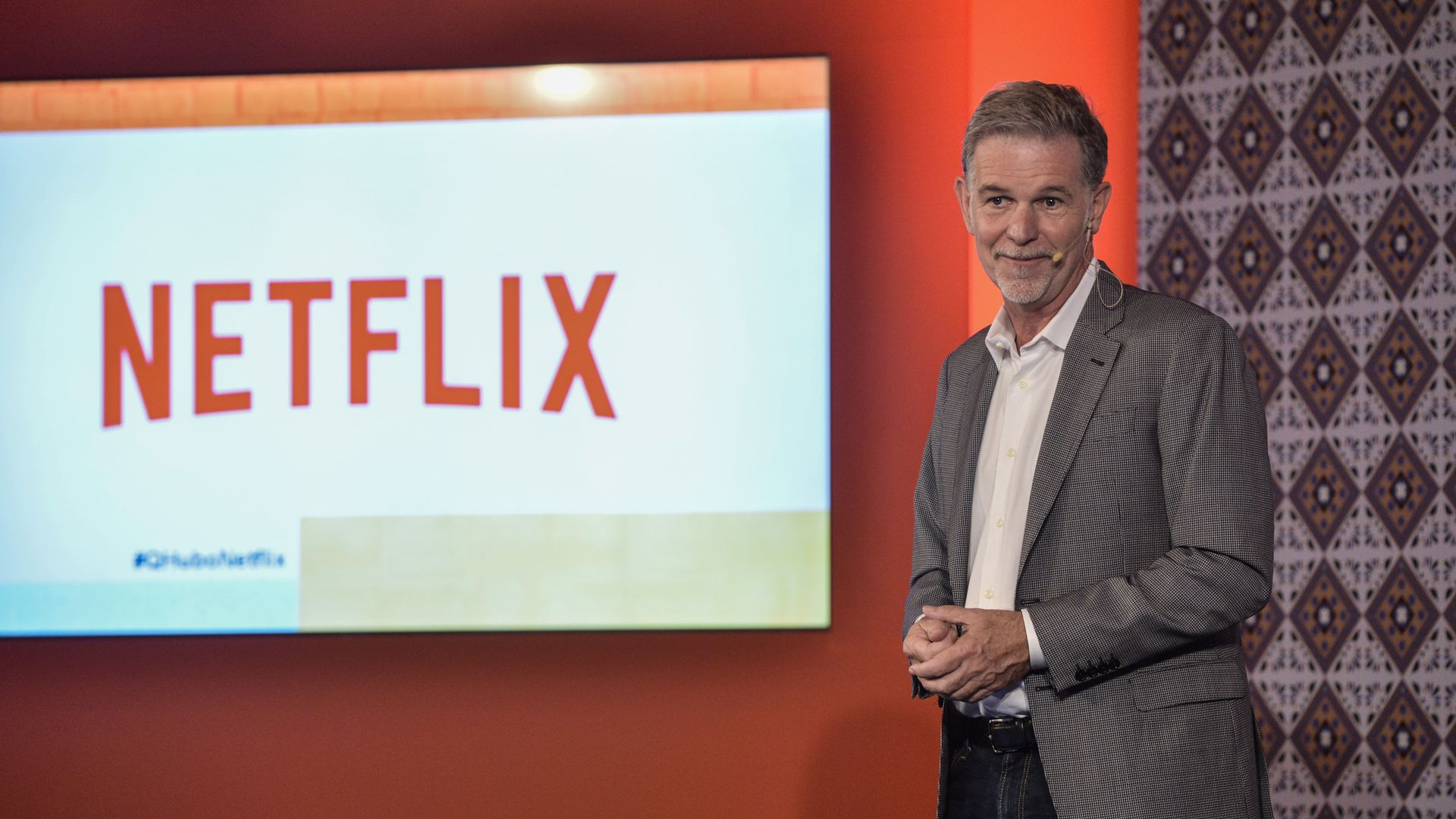 Reed Hastings standing on a stage with the Netflix logo on a screen in the background.