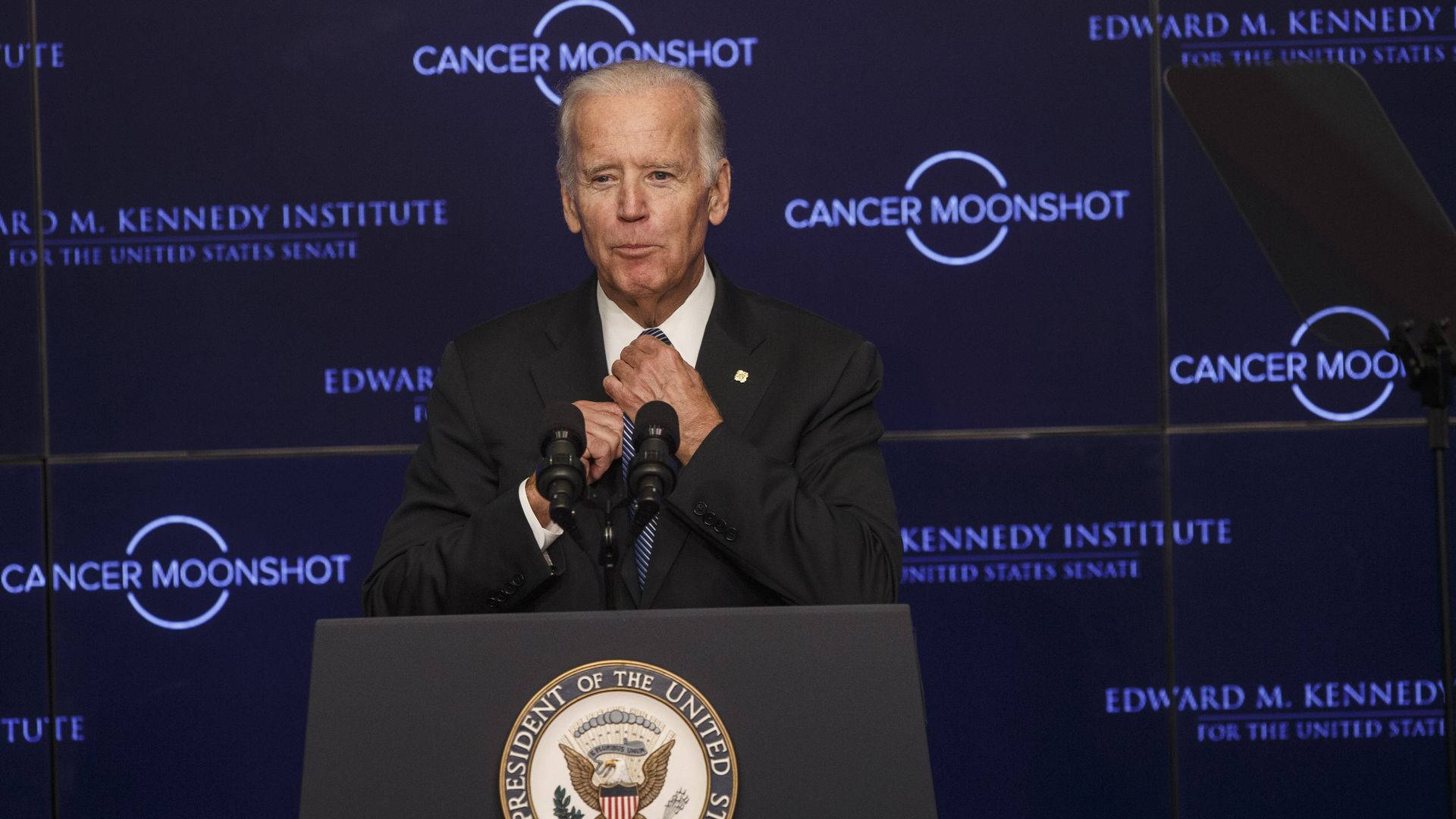 Joe Biden adjusts his tie while standing at a podium to speak