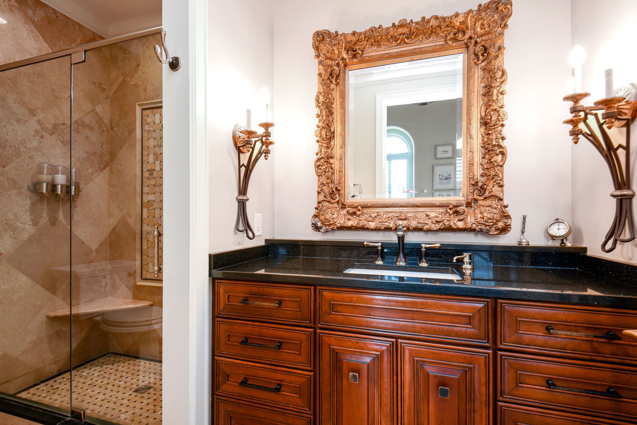 A bathroom with dark brown cabinets and a gold mirror.