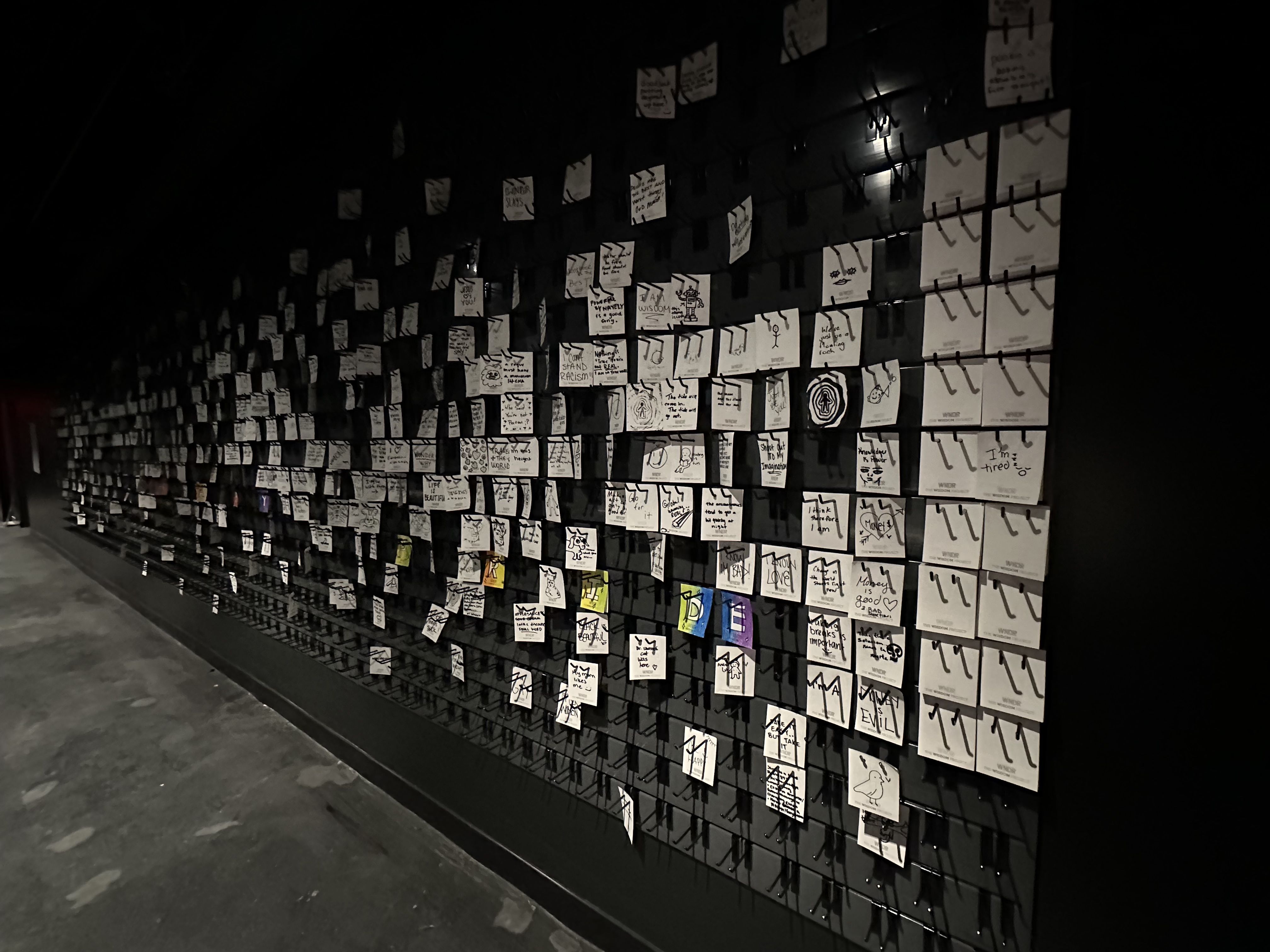 A wall full of white notes with messages in sharpie as part of the WNDR Museum's "The Wisdom Project," where people answer "what are they sure that they know" as an interactive exhibit.