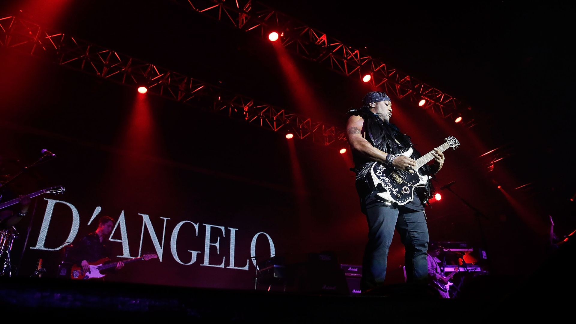 A man performing onstage with a guitar in front of a screen that says "D'ANGELO"