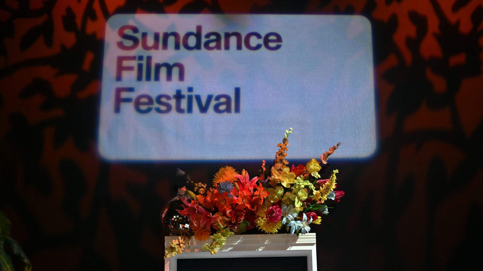 A screen reads "Sundance Film Festival" above a small table holding a bouquet of flowers.