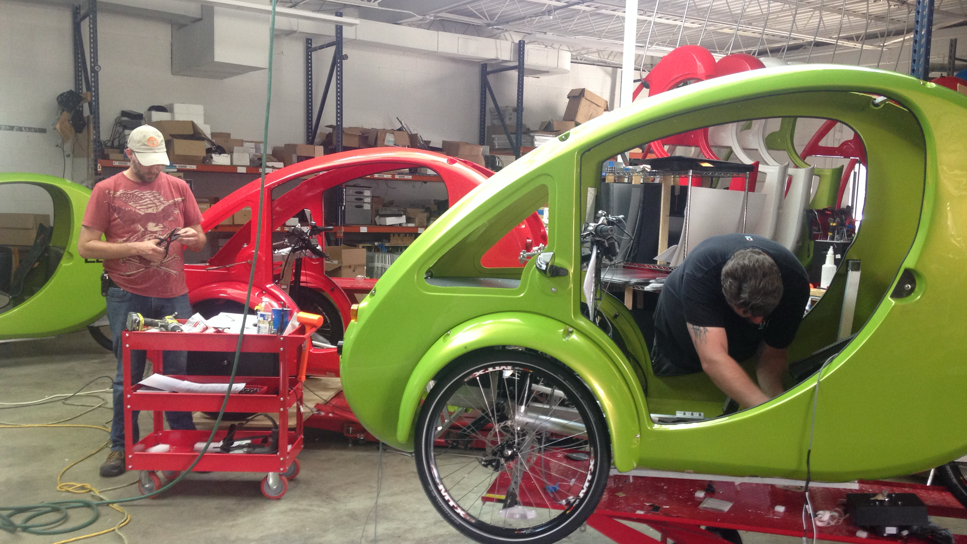 Workers in a garage assemble red and green Elf bicycle pods.