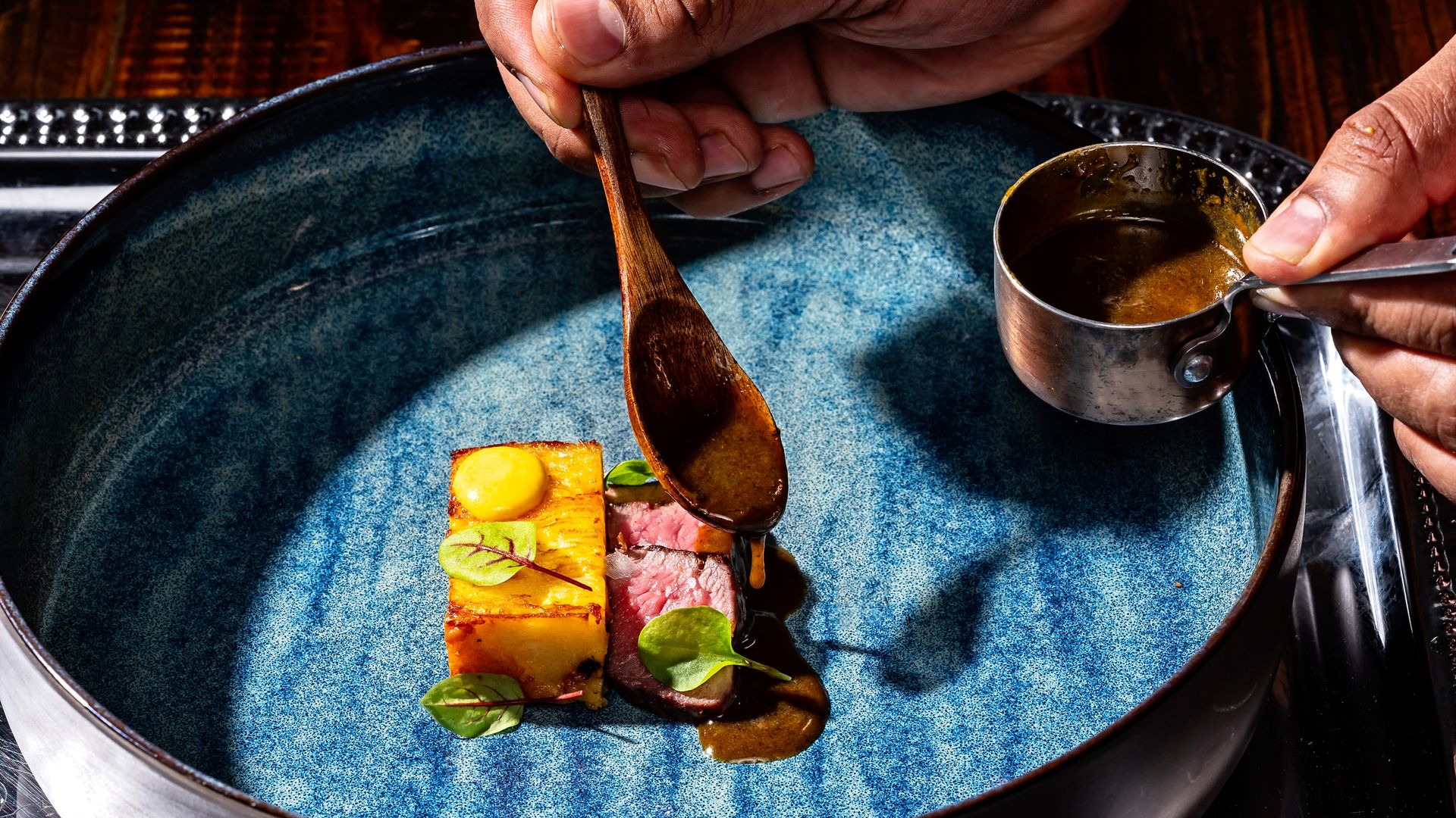 Steak and potatoes served in mini, fine-dining style servings on a big blue ceramic plate.