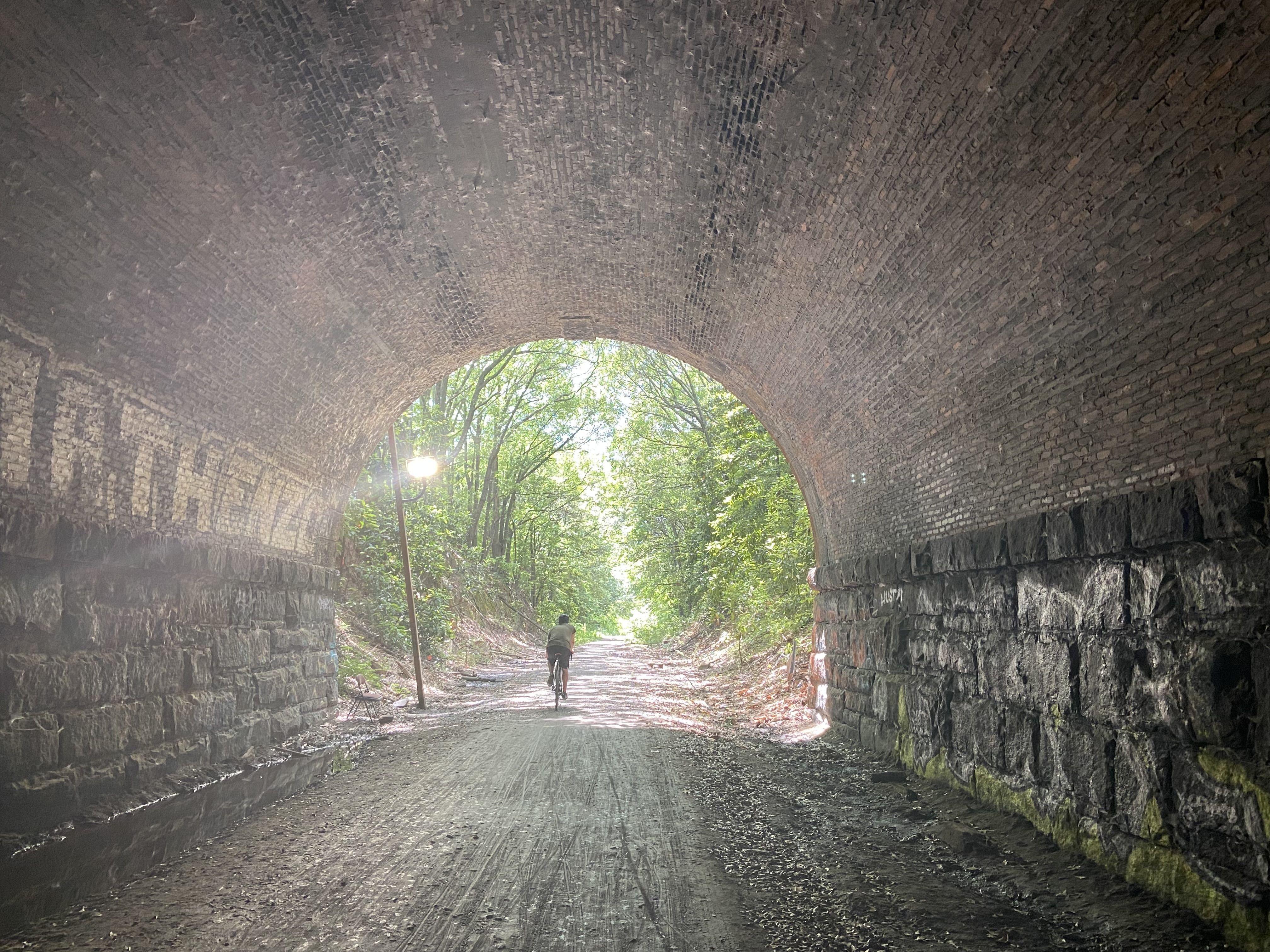 A bicyclist pedals on a gravel path passing through a tunnel with a rounded arch
