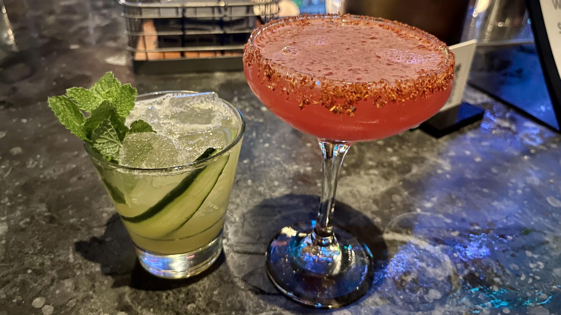 A cucumber cocktail garnished with mint in a short glass, left. A watermelon cocktail with spicy tajin on the rim, right.