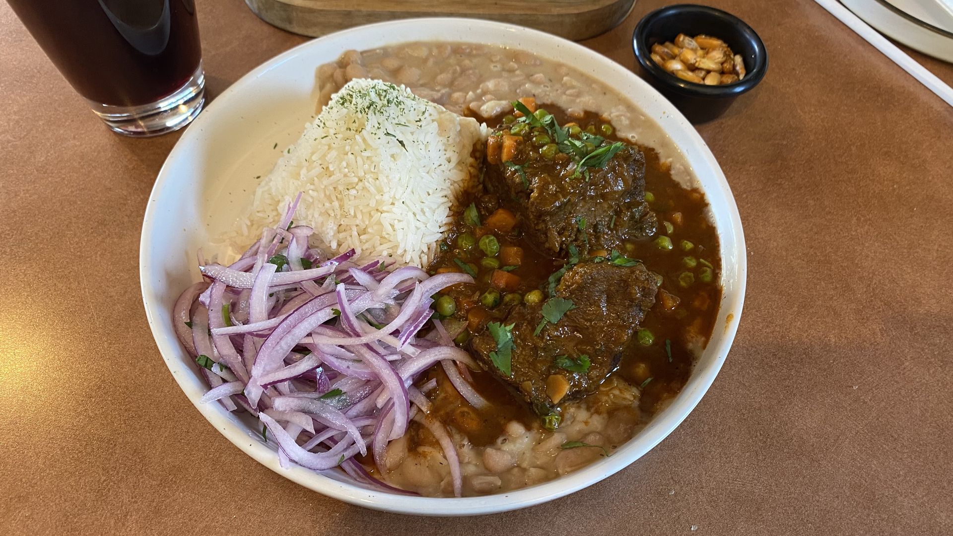 A white plate filled with beef stew, a rice pilaf, beans and diced onions.