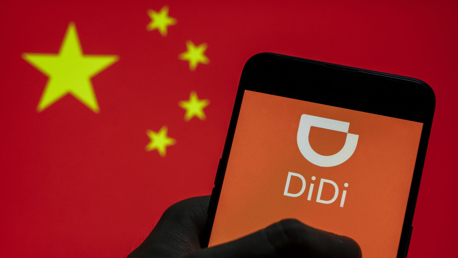Picture of a hand holding a smartphone displaying the DiDi logo with a Chinese flag in the background