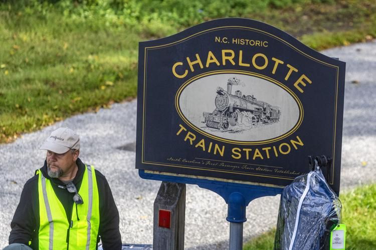 Blue Charlotte sign for a historic train station with a film crew worker standing to the left in an yellow vest. 
