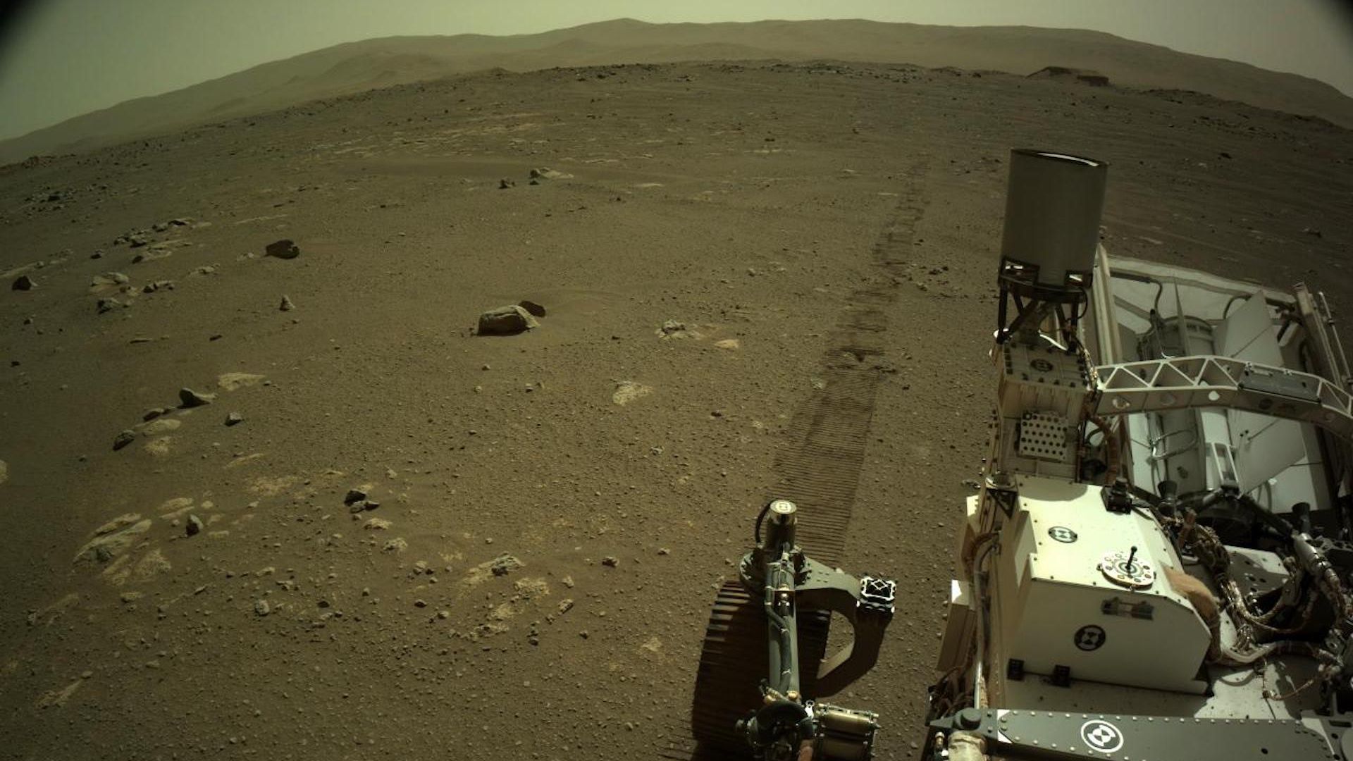 Tracks trailing out behind the Perseverance rover with rising mountains in the distance on Mars