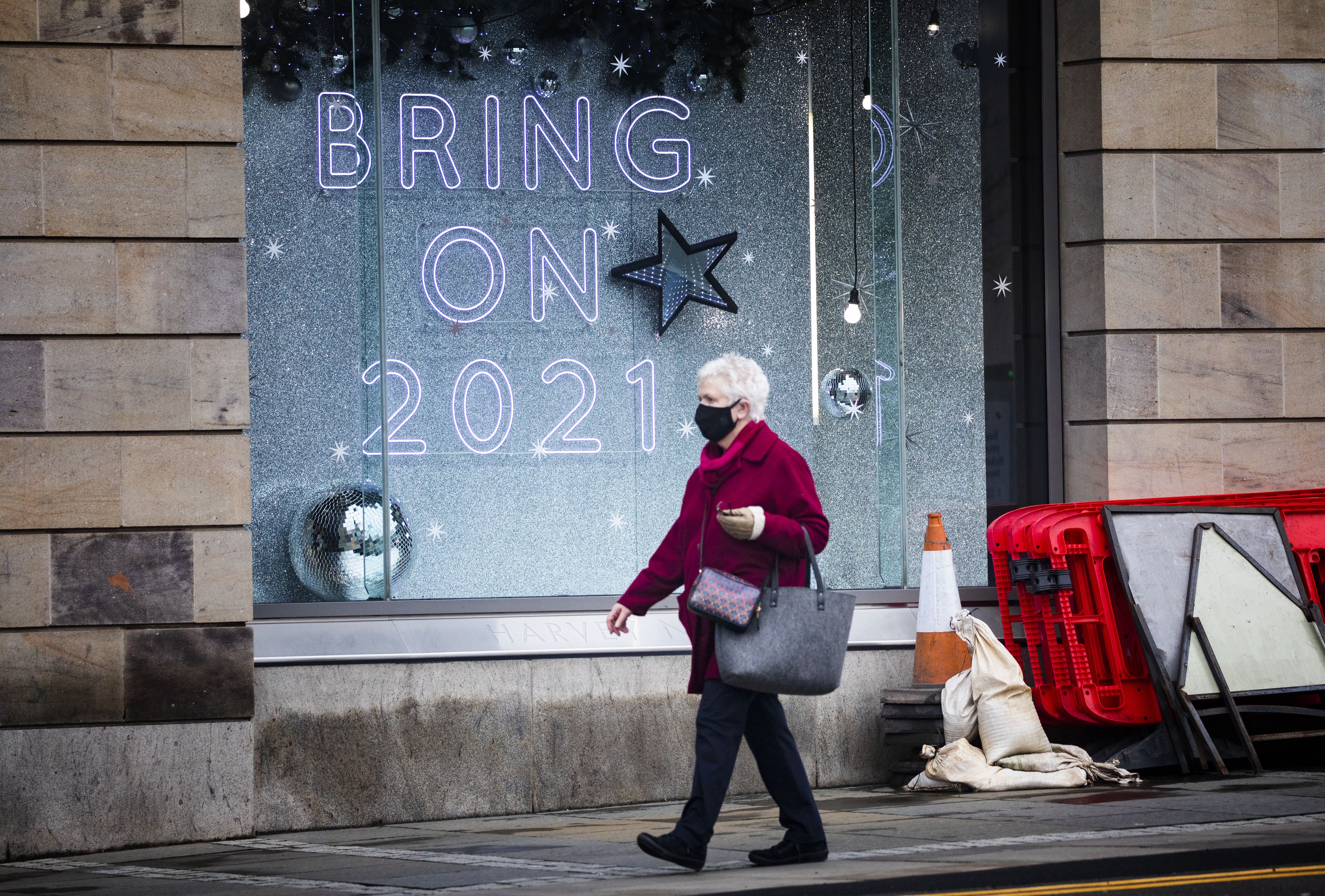 A shopper wearing a protective face mask walks past a shop sign that read "Bring On 2021" in Edinburgh city centre.