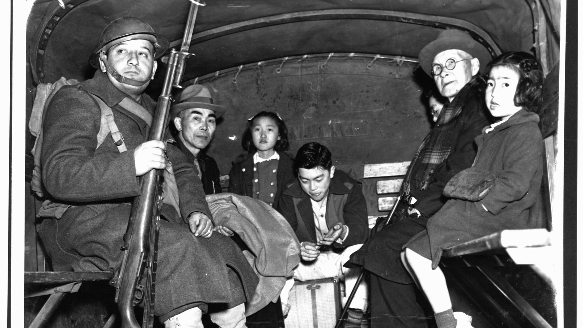 A soldier escorts several Japanese American children and a pastor in the back of a truck during their evacuation from Bainbridge Island to an internment center. 1942.