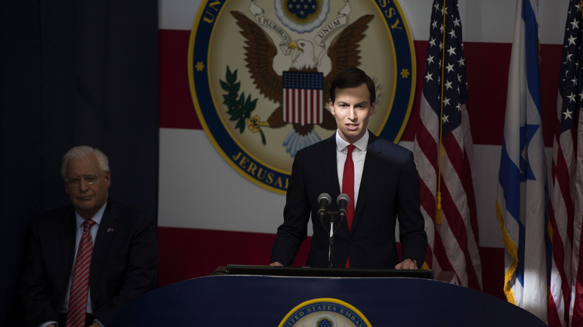 Jared Kushner behind a podium in a dimly lit room