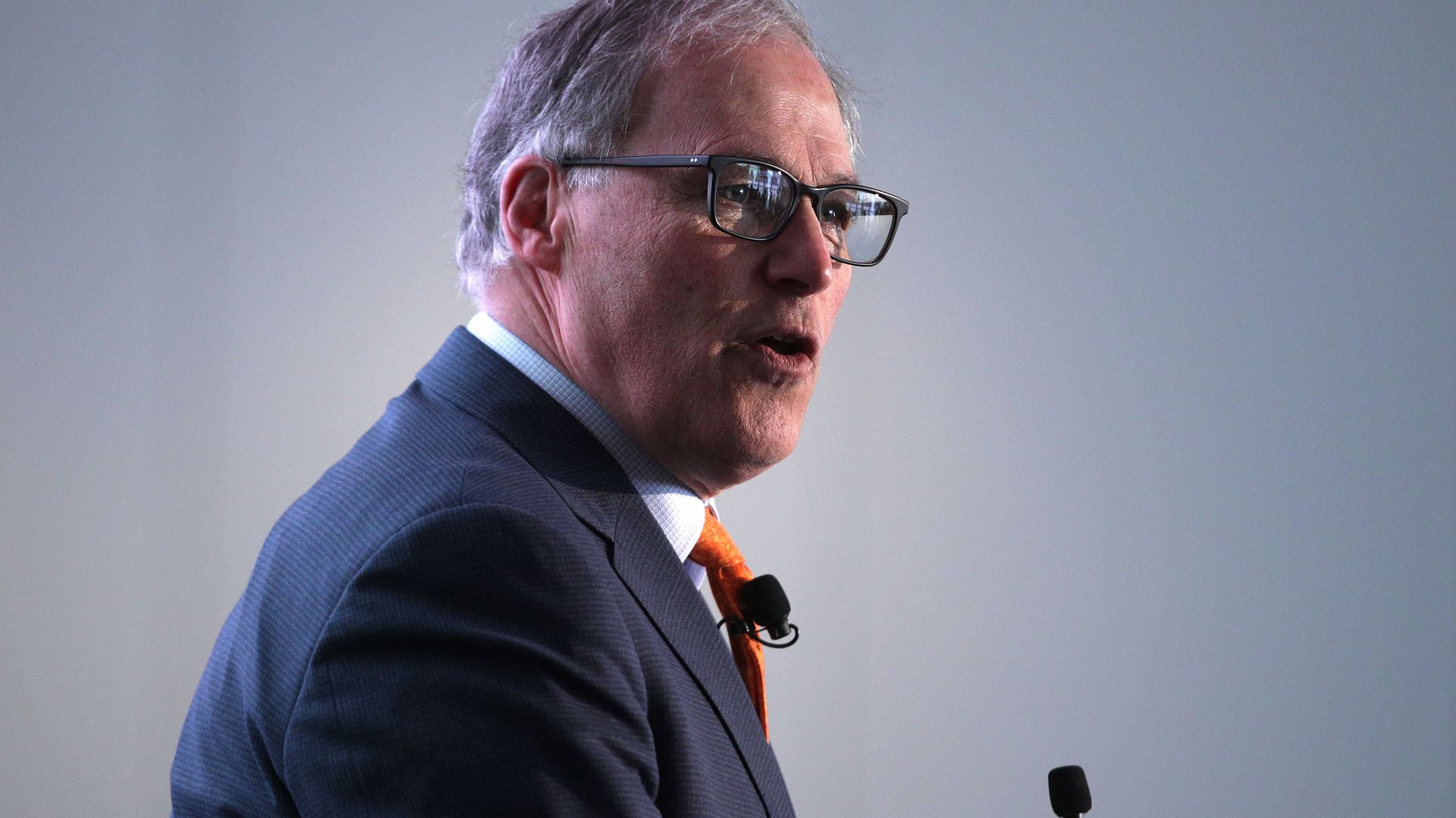 Gov. Jay Inslee faces to the right and speaks in a suit in this image. He's wearing glasses.