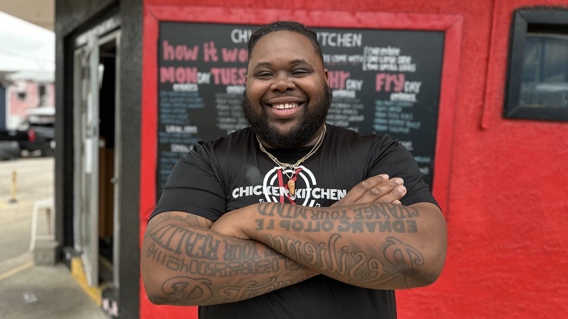 Marlon "Chicken"Williams smiles and poses for a photo in front of his restaurant while crossing his arms.