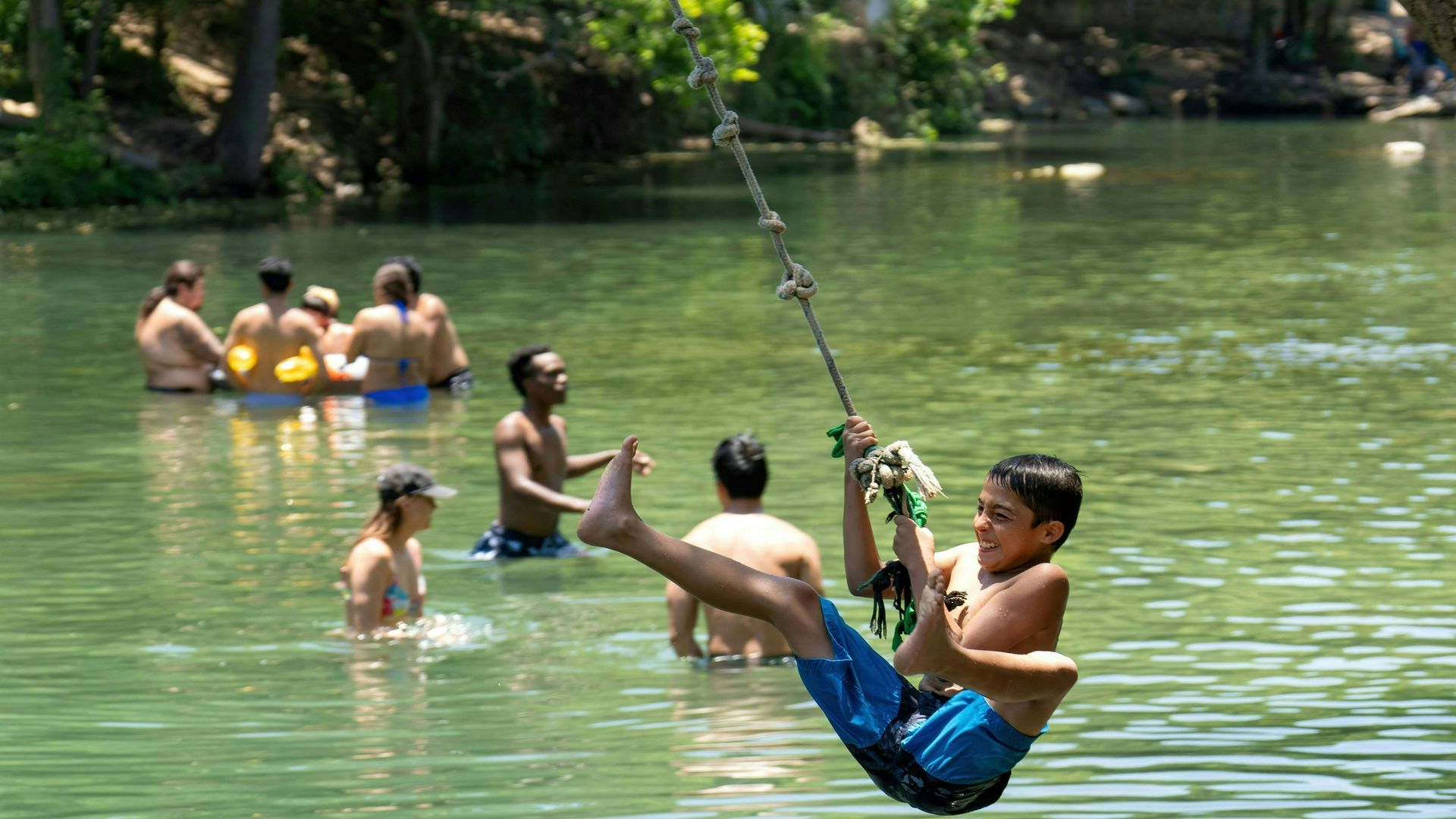 A photo of a person on a rope swing with swimmers in the background.