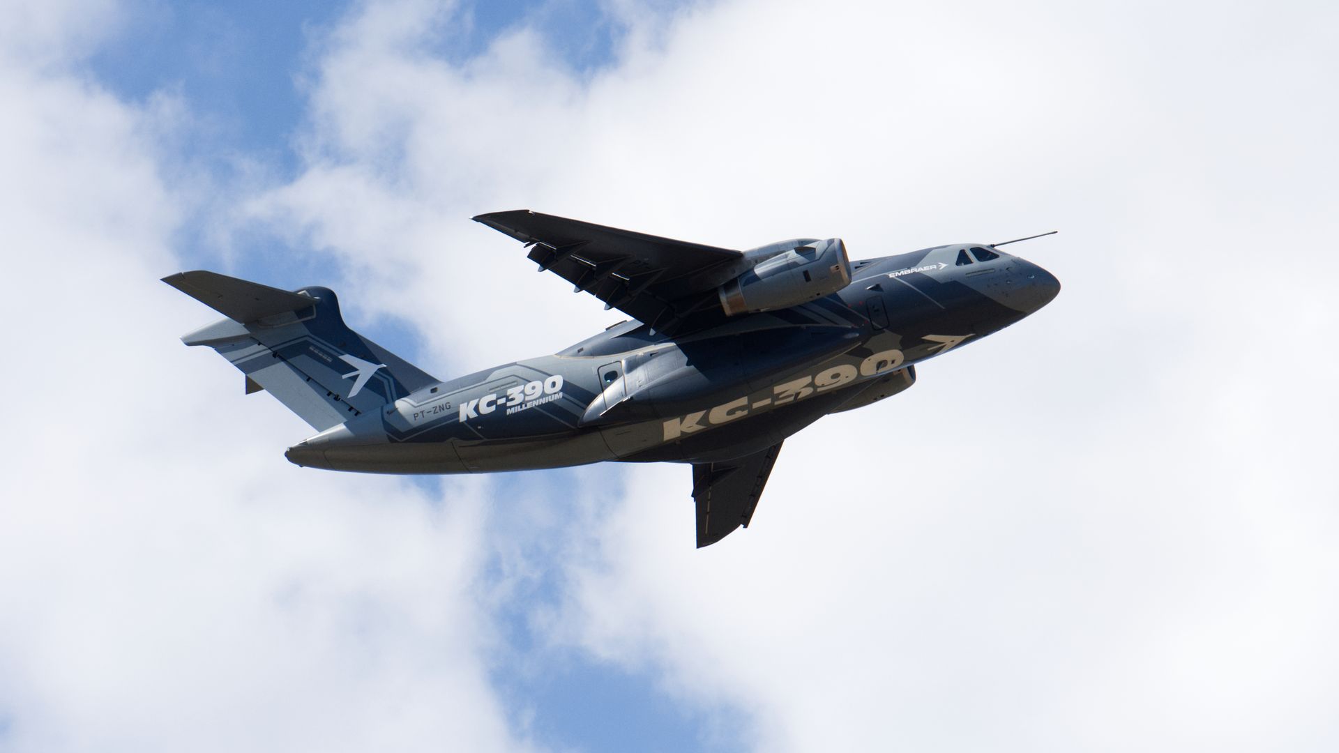 A large transport-and-refueling aircraft flies through cloudy-blue skies.