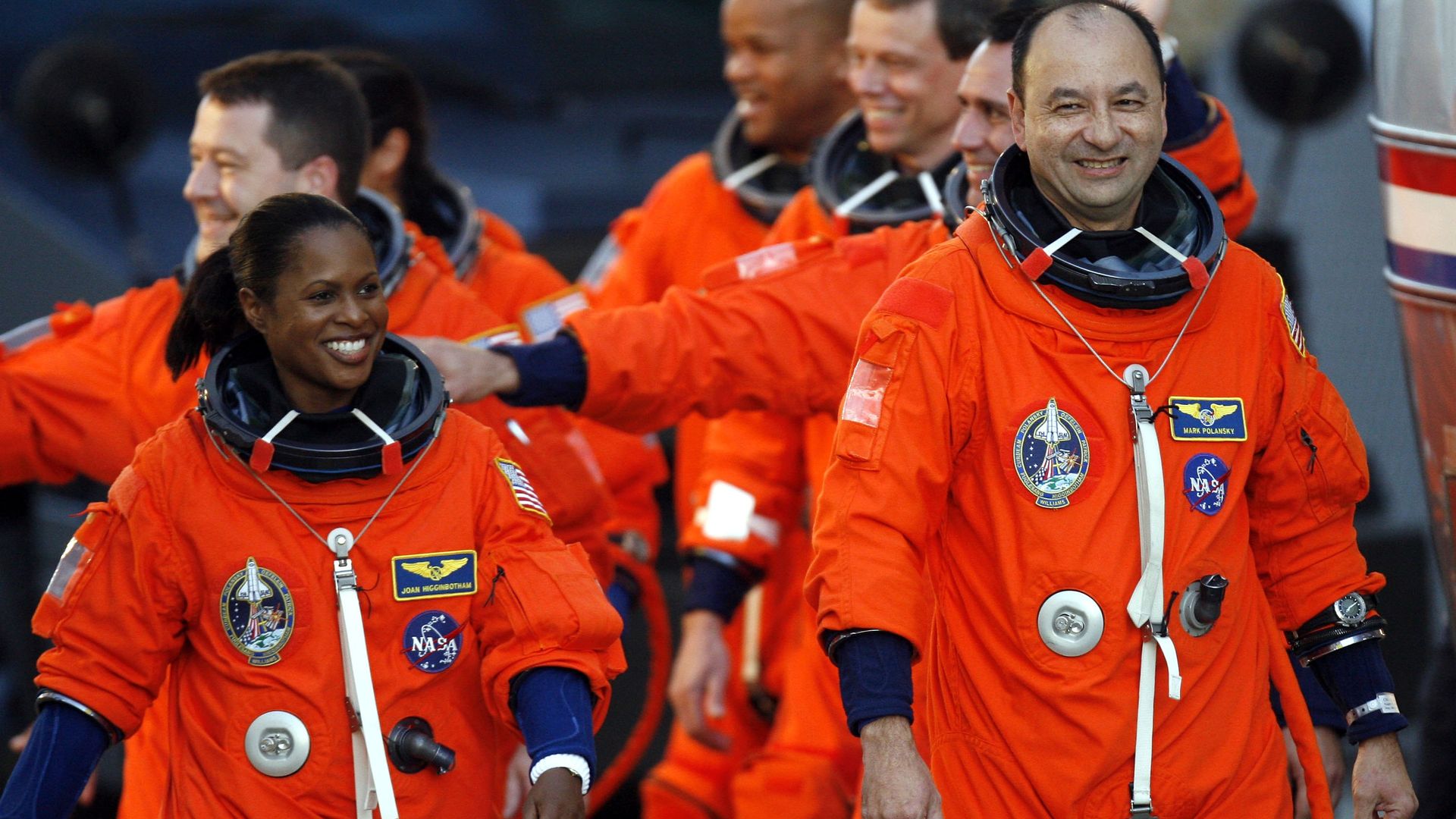 NASA astronauts in orange suits walk to a launch event for space shuttle Discovery in 2006. On the left is Joan Higginbotham