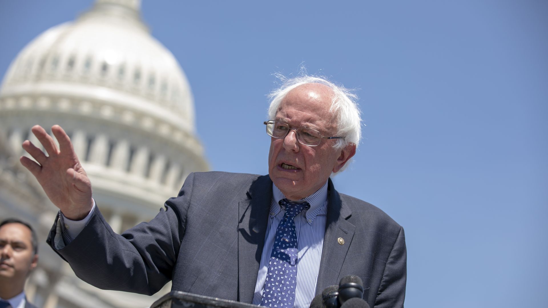 Sanders gesturing as he speaks, behind a podium