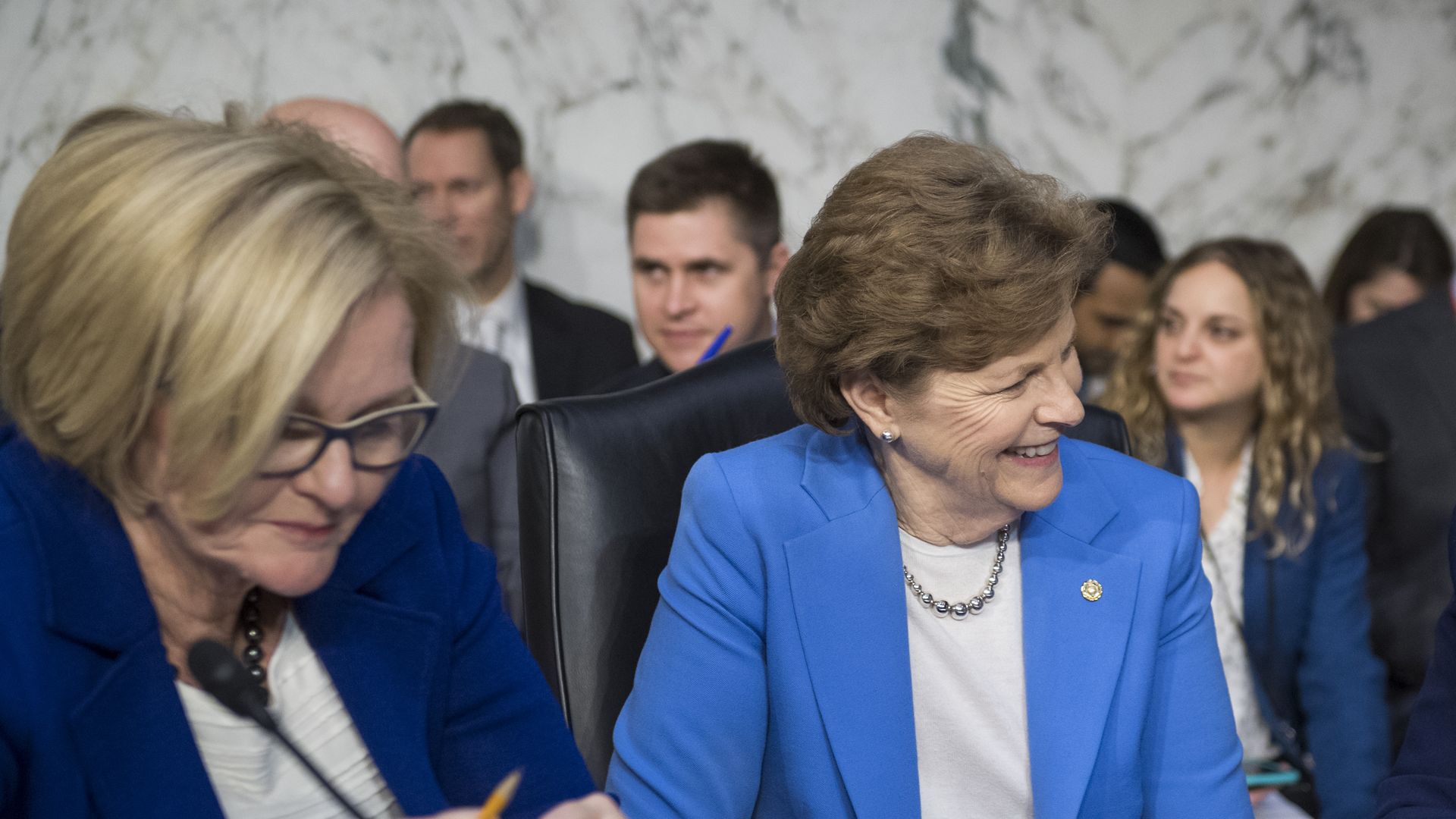 Senator McCaskill looks down at a desk and Senator Shaheen smiles.