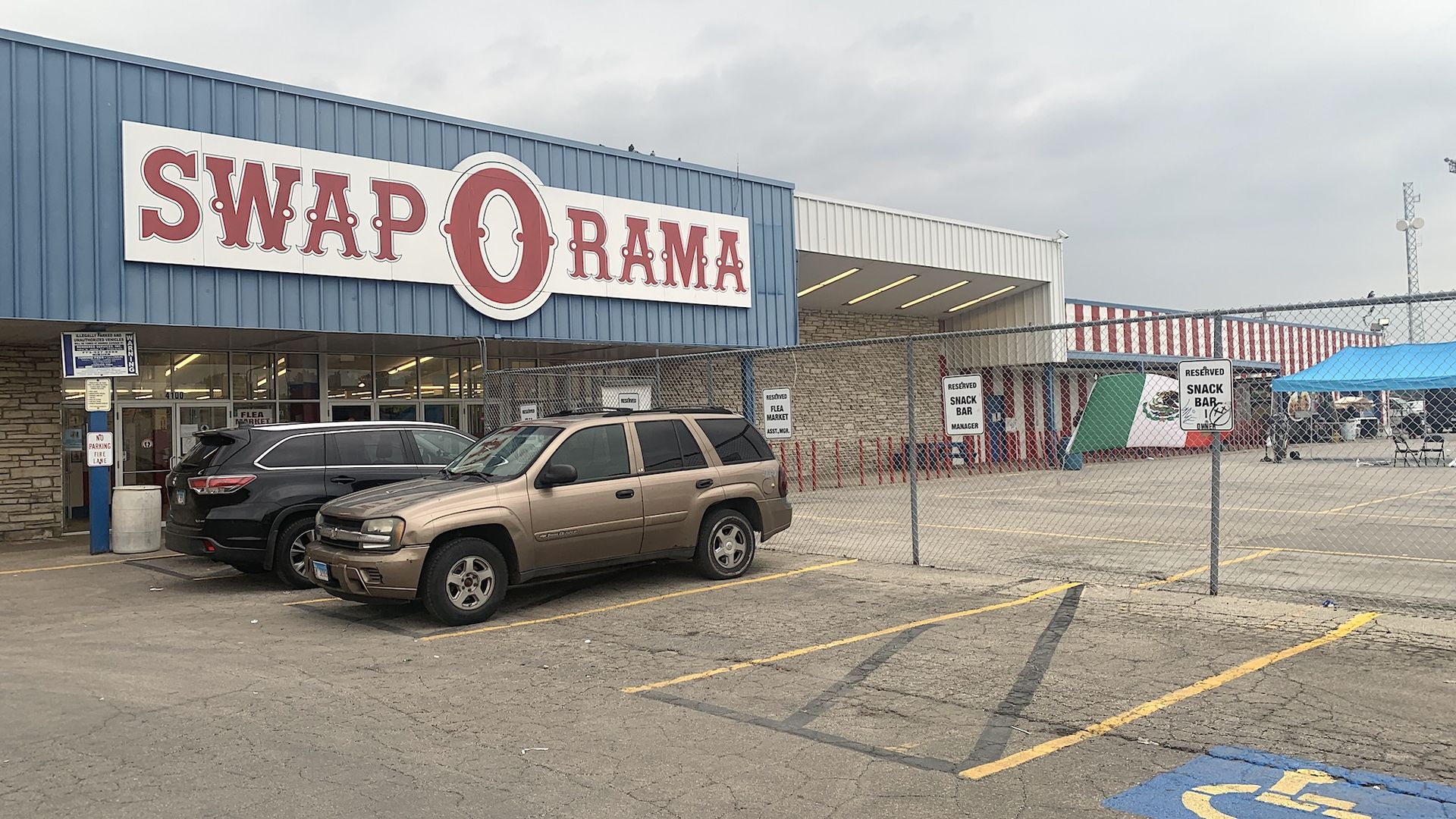 Mall sign reading "Swap-O-Rama" in red letters on a blue background, Mexico flag attached to fence, waving in the wind.