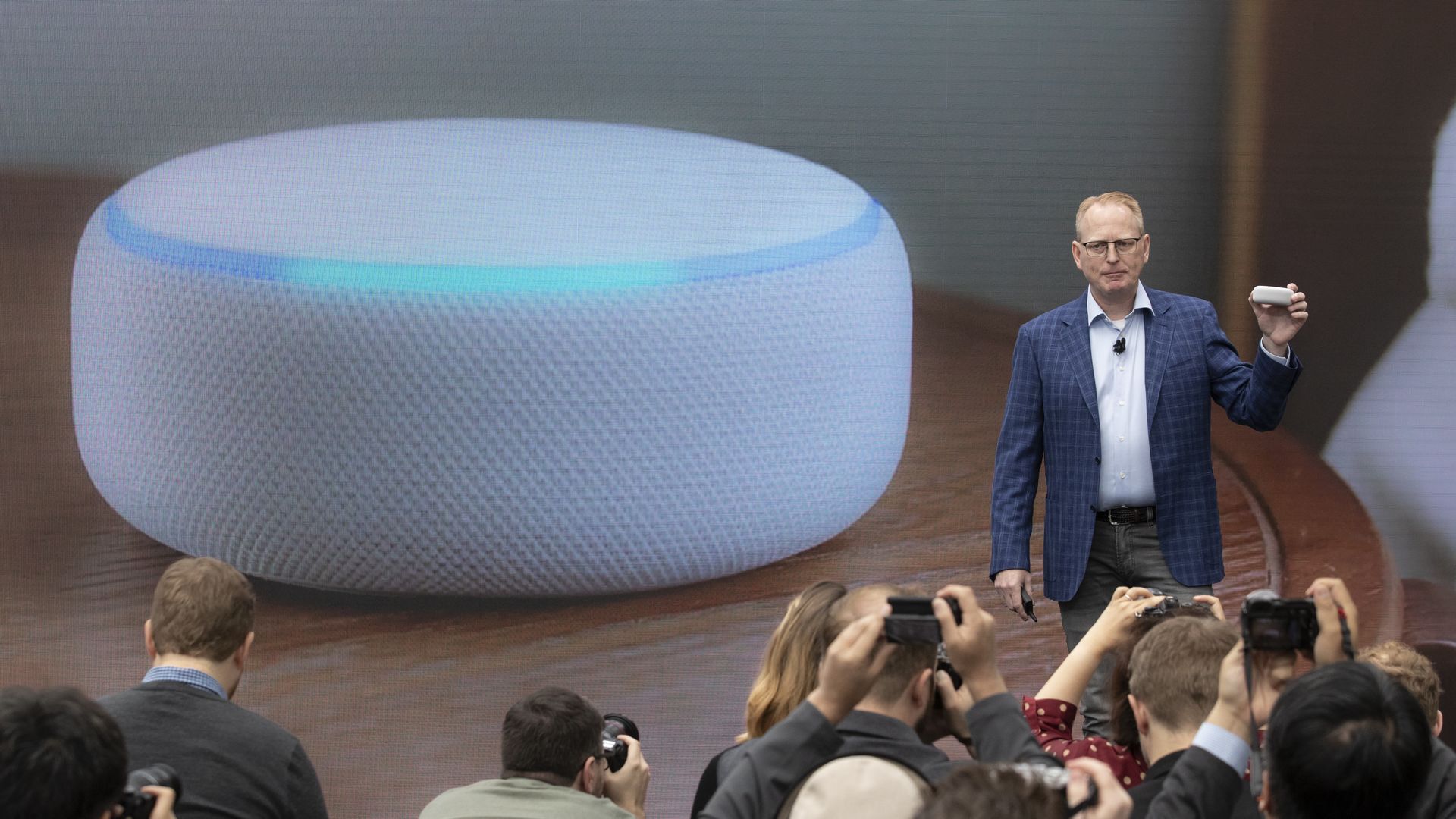 Photo of Amazon executive Dave Limp talking to an audience standing next to photo of a smart speaker