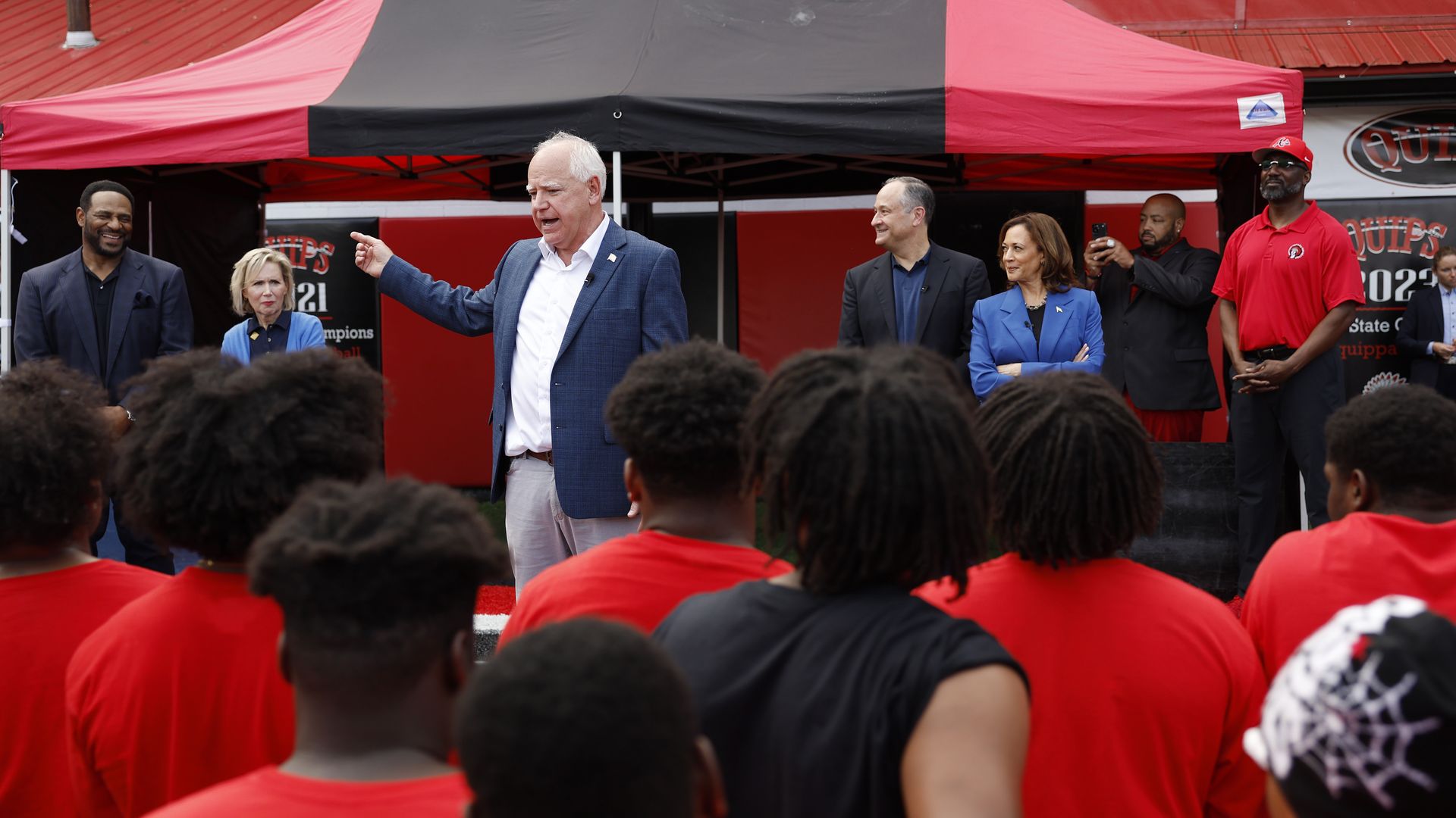 Minnesota Gov. Tim Walz, Vice President Kamala Harris and Second Gentleman Doug Emhoff speaking to a group of high school football players.