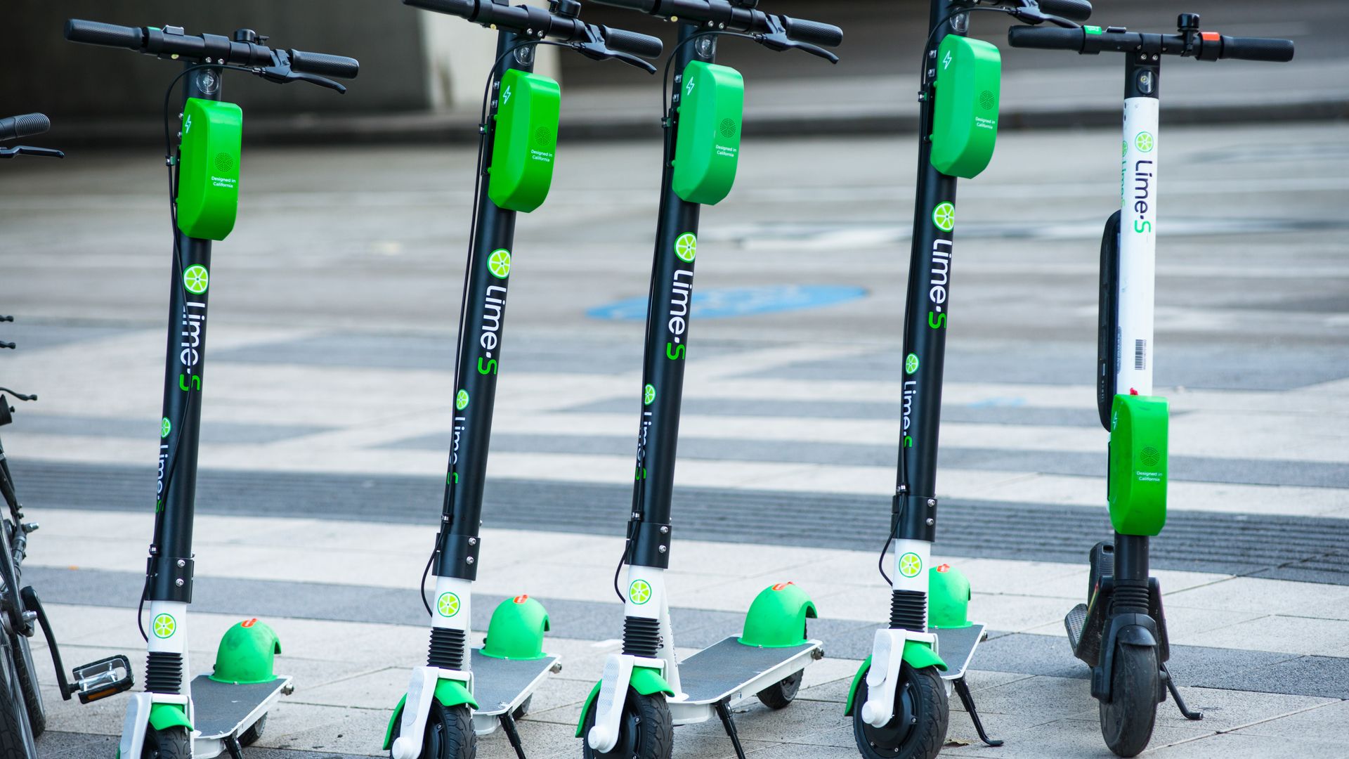 Line of Lime-S dockless electric scooters on a sidewalk, black poles with bright green battery boxes, lime-green branding, handlebars and wheels visible.