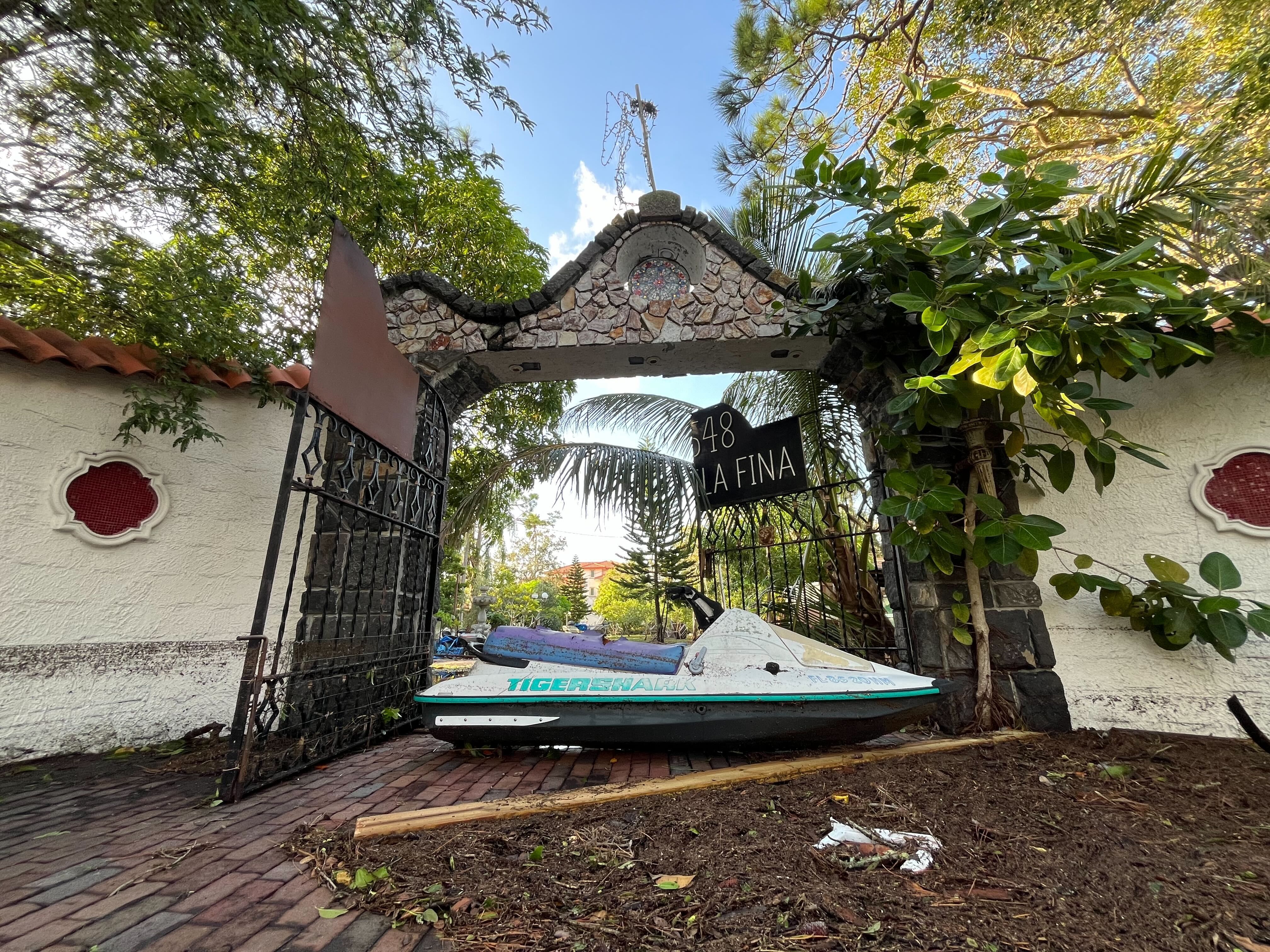 A jet ski on land in a driveway in front of an iron gate and a white stone wall.
