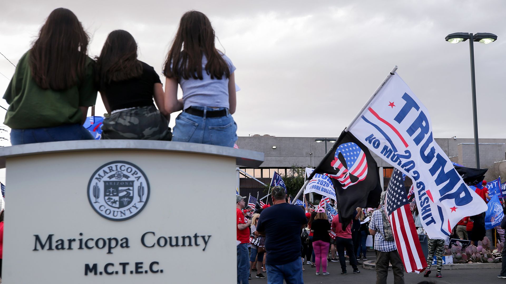 A signt hat says "maricopa county" with A Trump flag in the background.