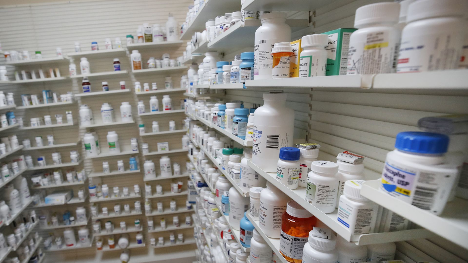 The back of a pharmacy, with shelves filled with bottles of pills and medications.